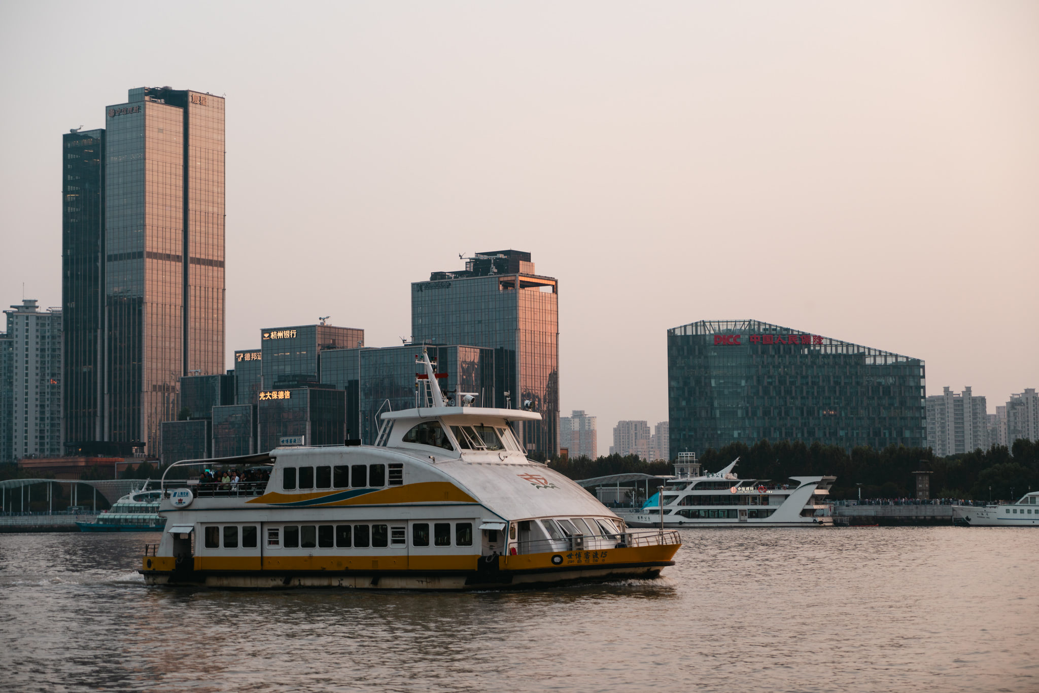Cruise boat on river with city skyline at dusk.