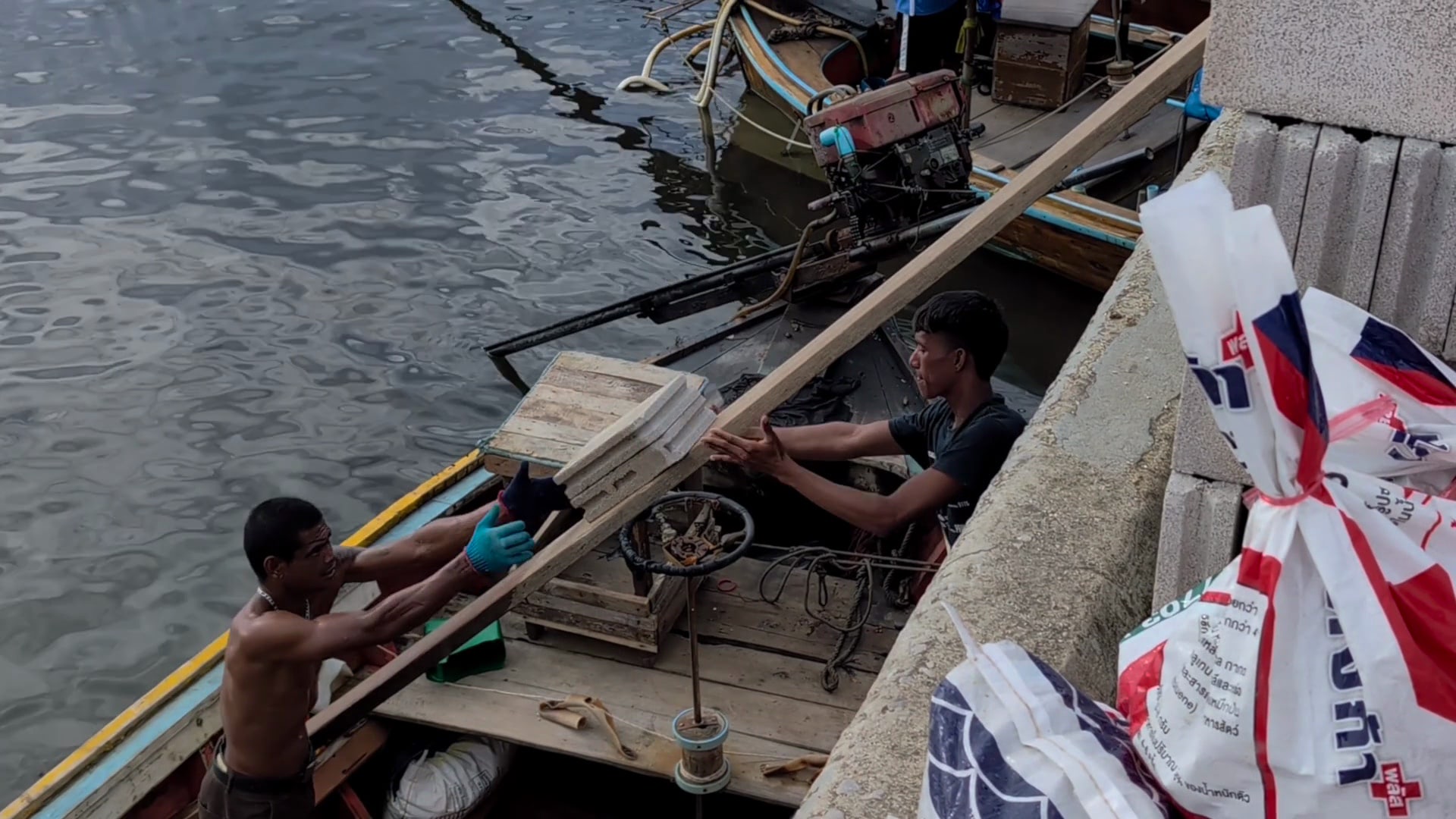 Two men load bricks onto a boat in Thailand.