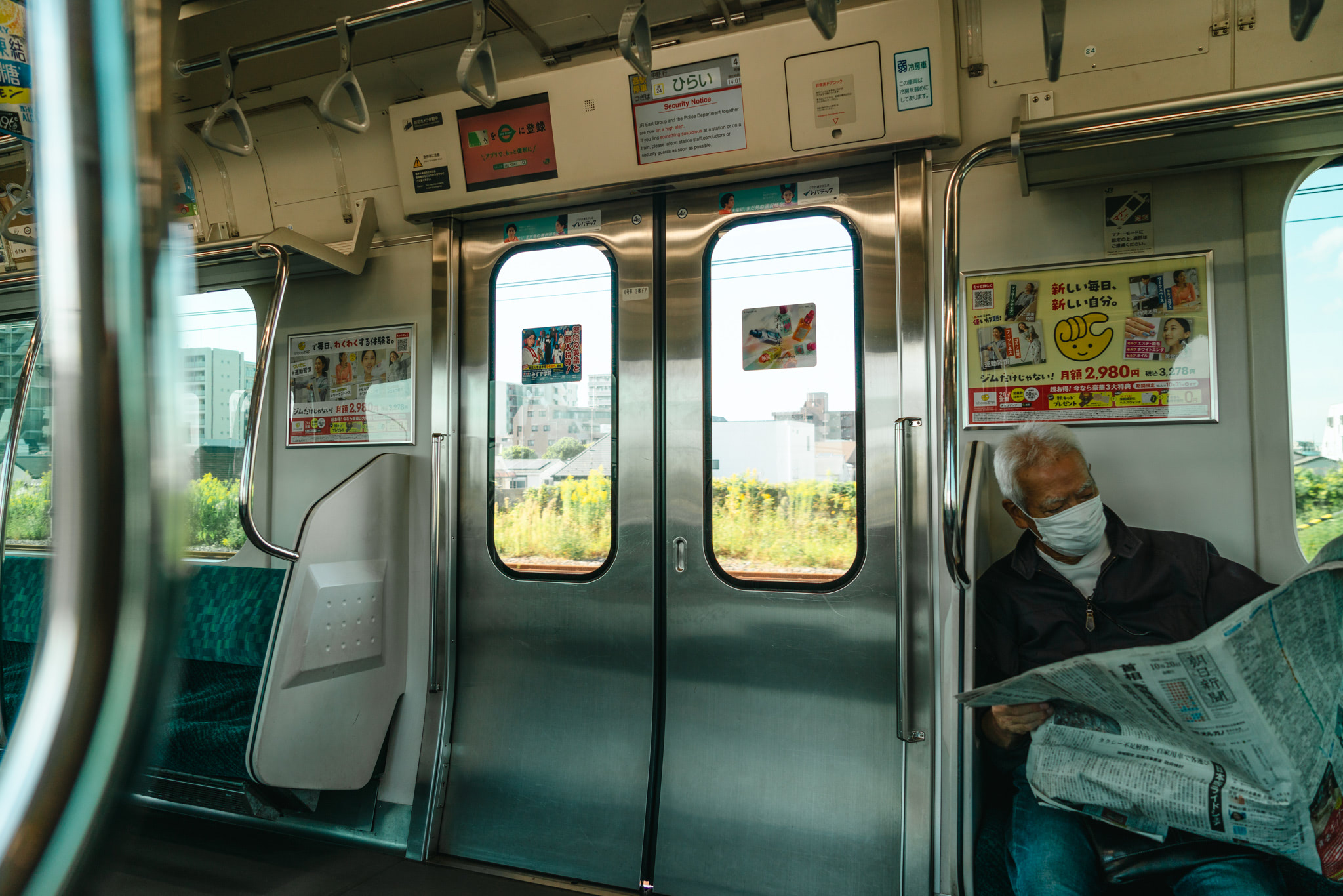 Man wearing a facemask reads a newspaper on a Japanese train.