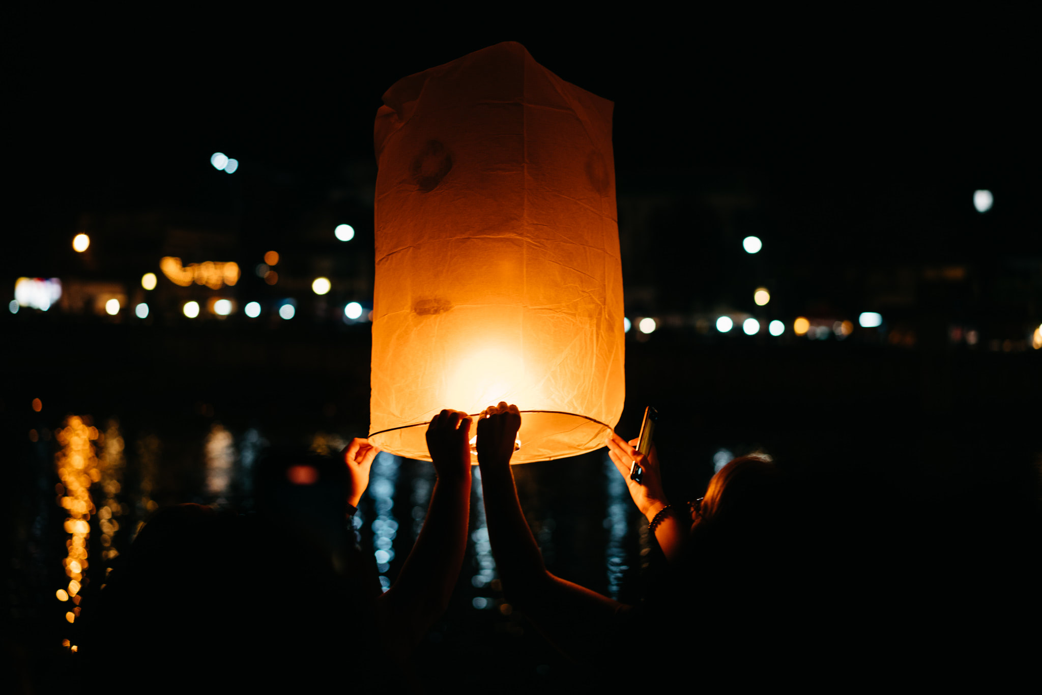 Two people release a glowing sky lantern at night.