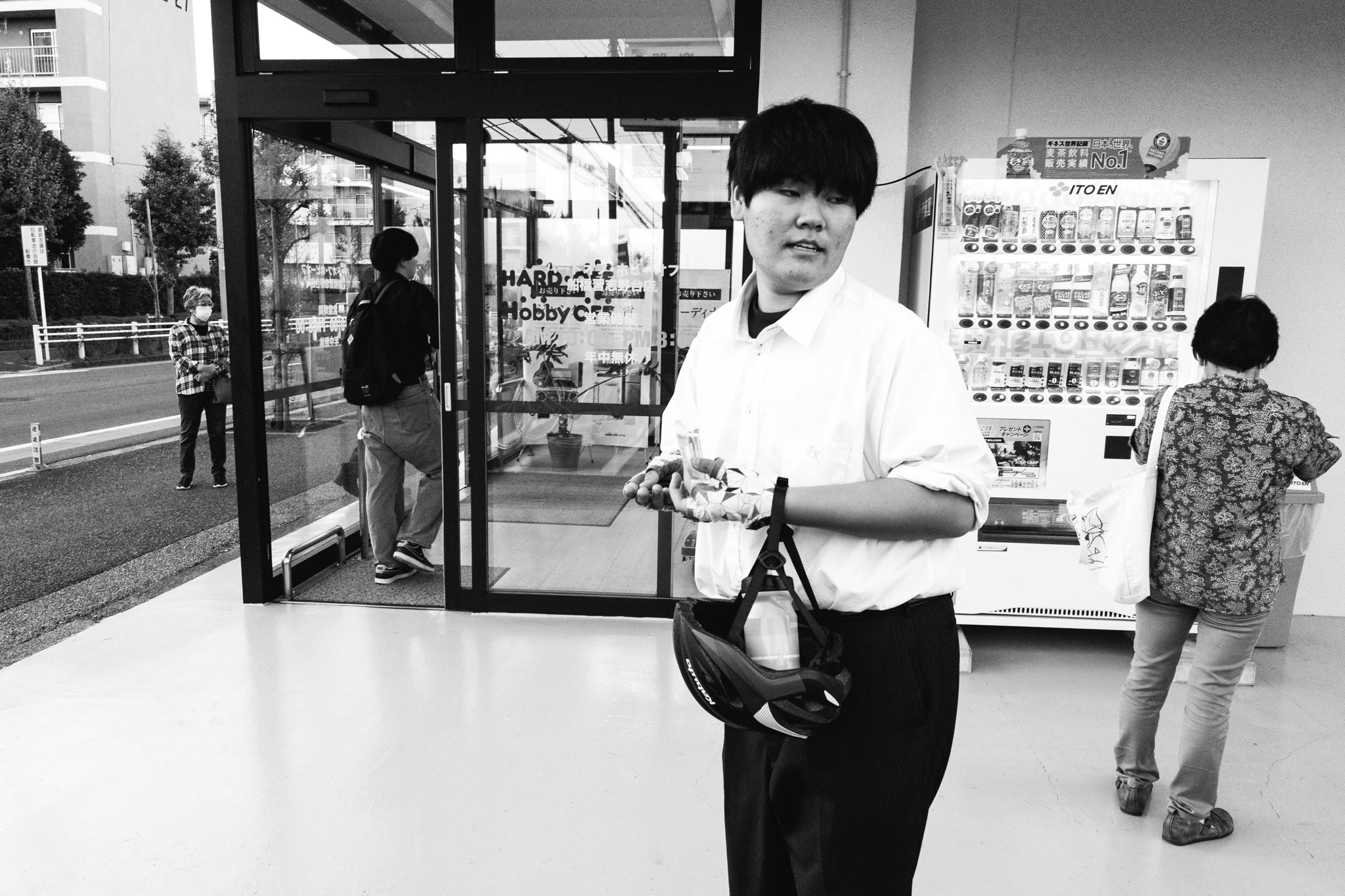 Black and white photo of a young man holding a bicycle helmet outside a shop.