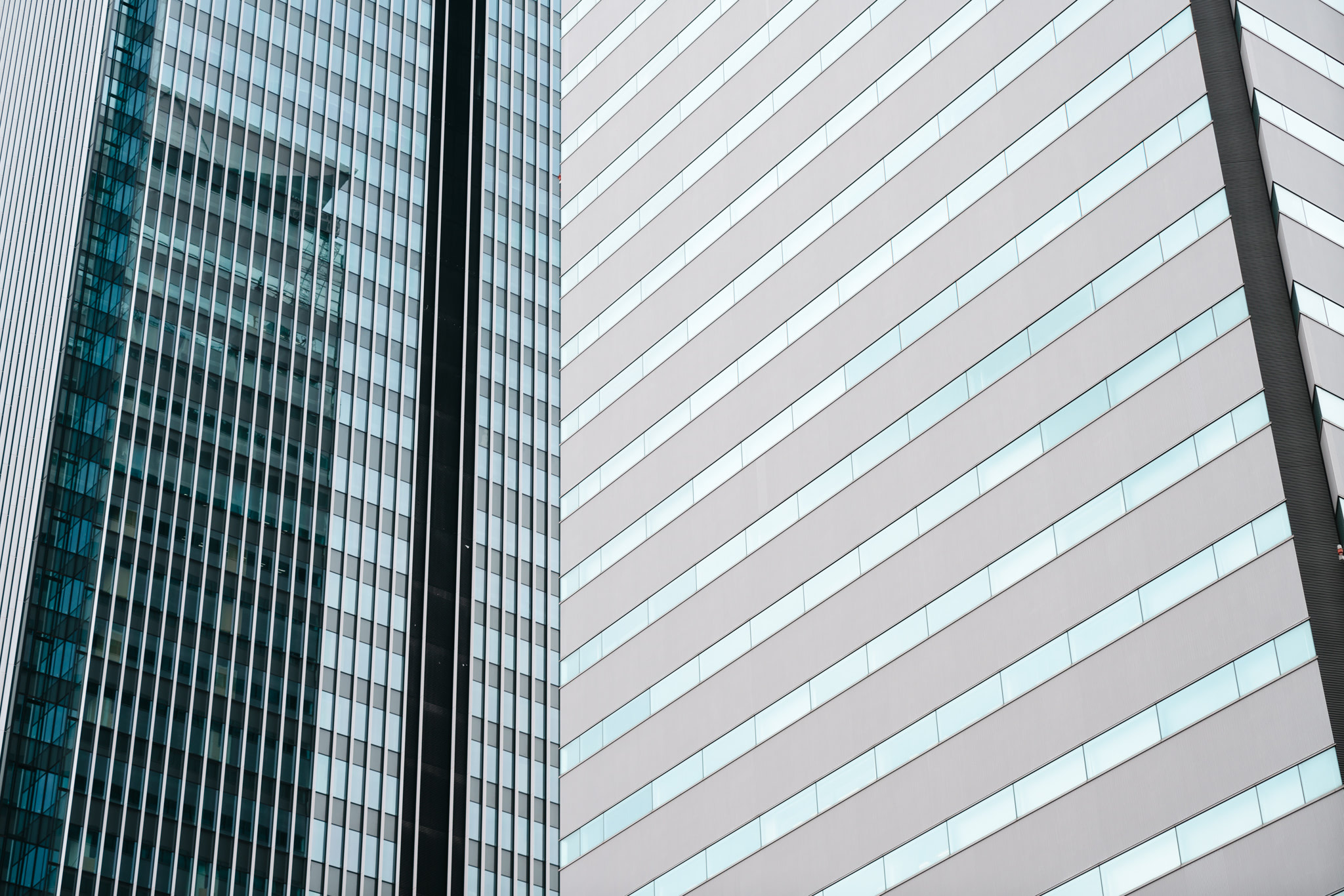 Close-up of two modern office buildings; one with glass and metal facade, the other with light gray panels and rectangular windows.
