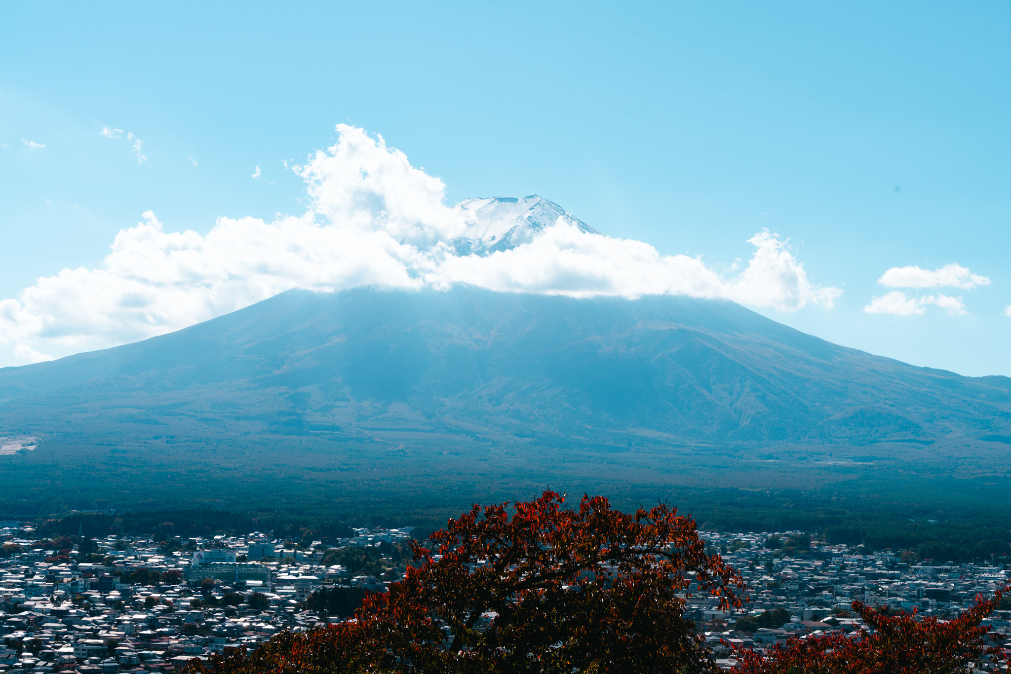 Mount Fuji with a partially cloudy sky, viewed from above a town.