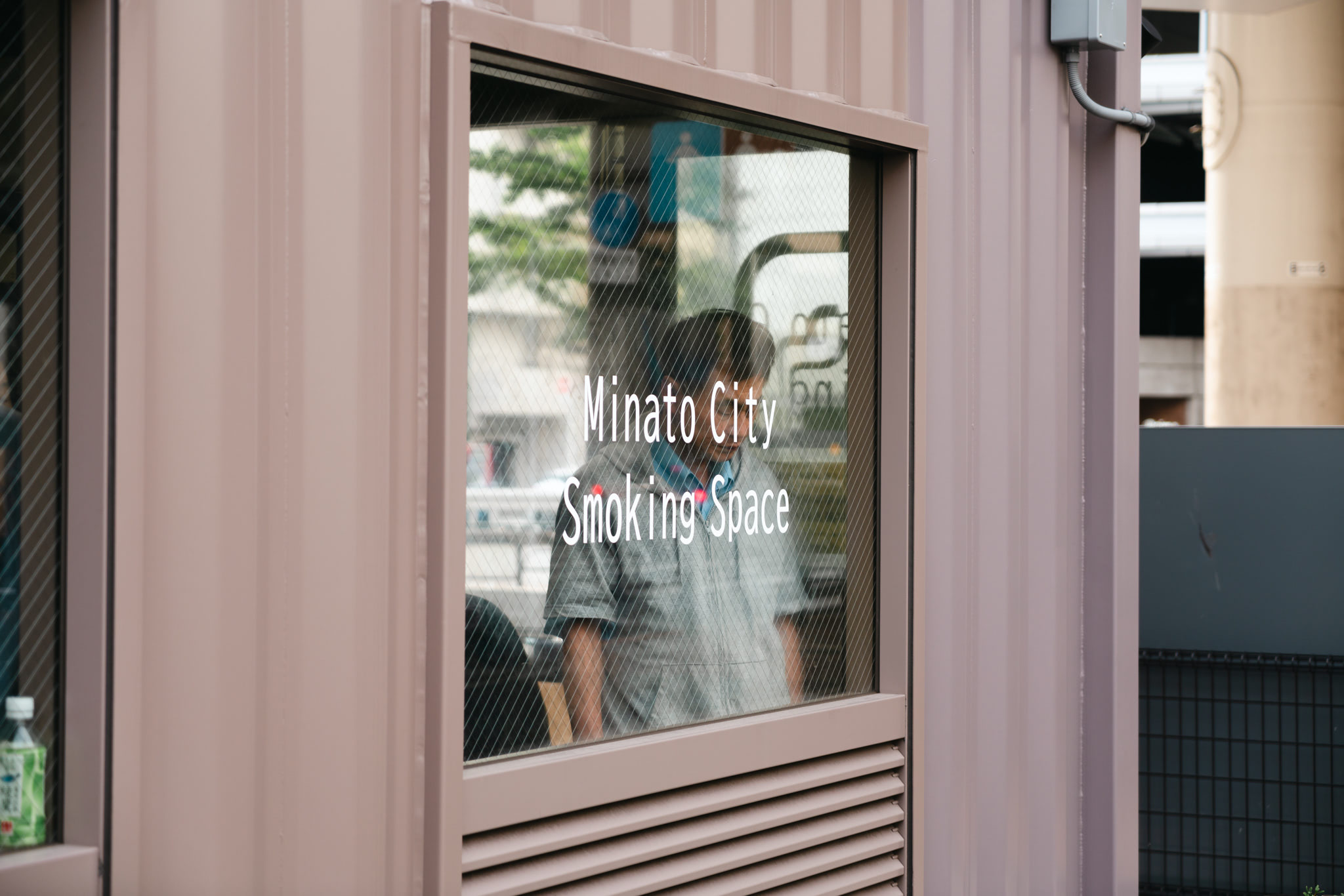 Minato City Smoking Space sign in a window, person inside.