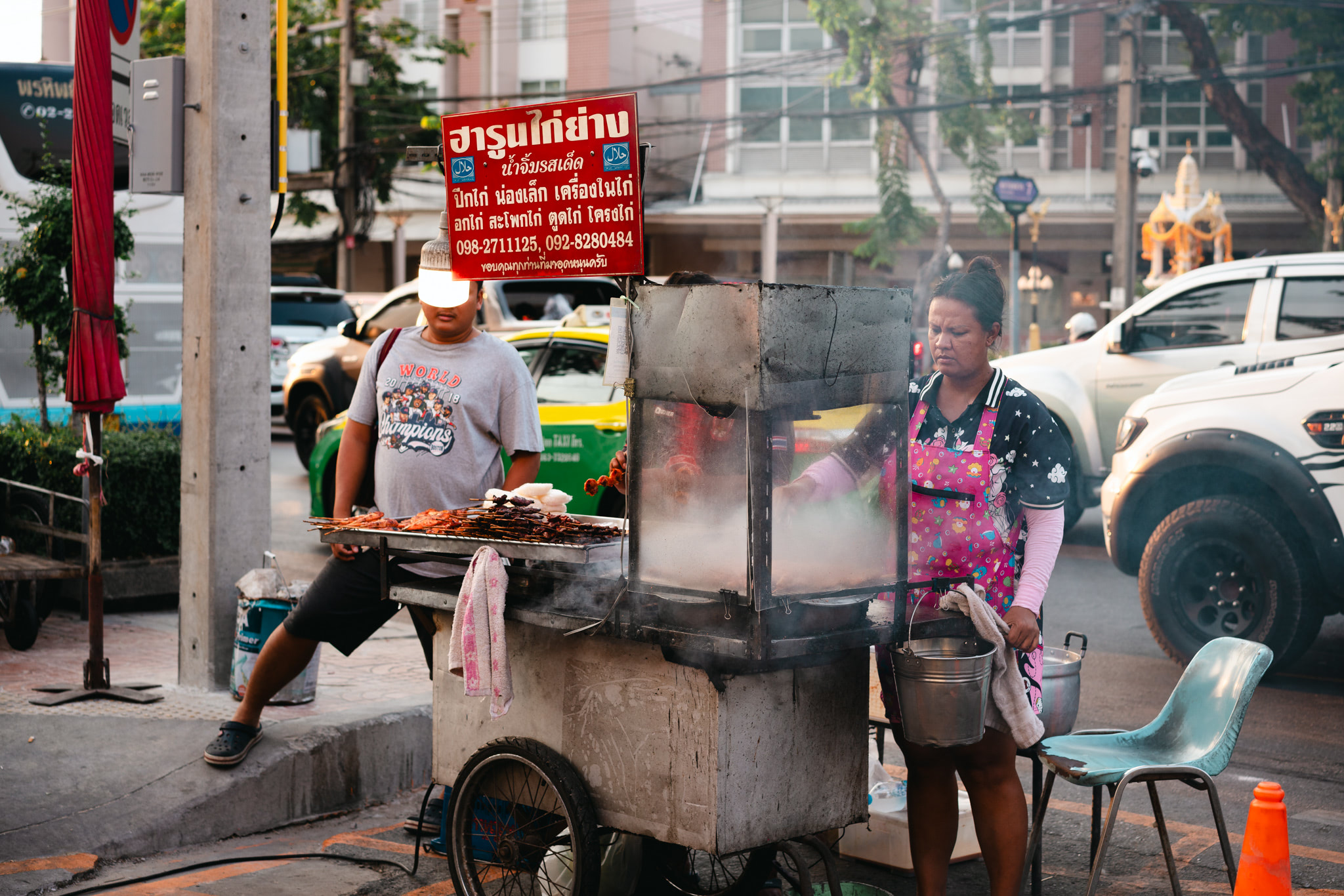 Bangkok street food vendor BBQ stand with two people cooking.