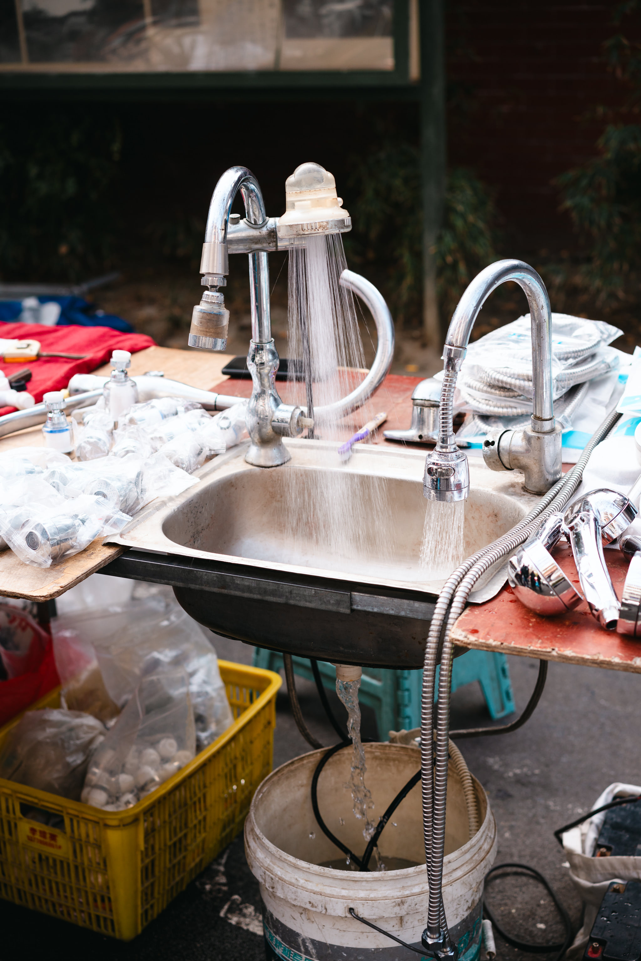 Water running from a sink and faucets at an outdoor plumbing stall in Chengdu.