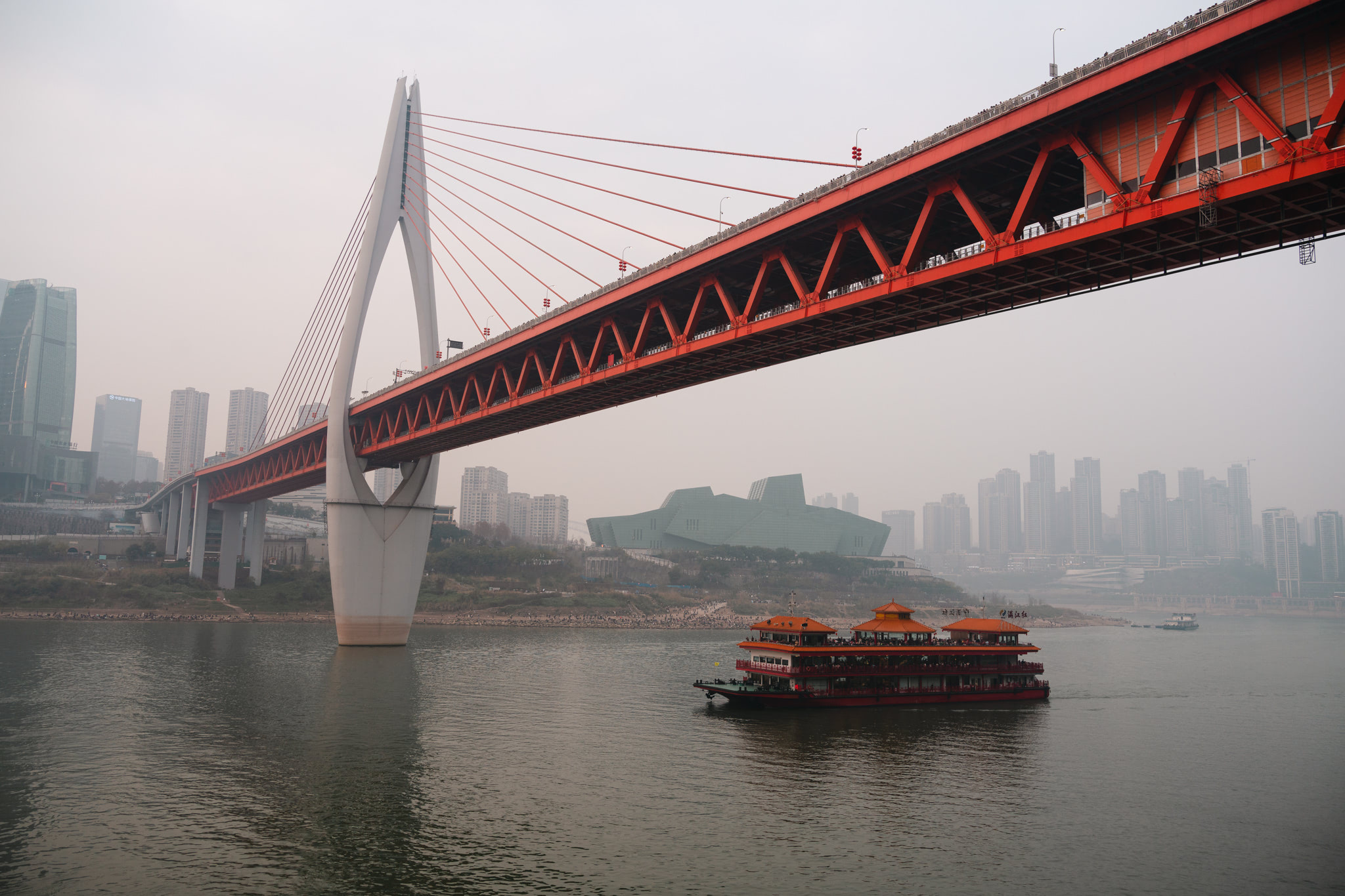 Chongqing cable-stayed bridge over river with boat and city skyline in background.