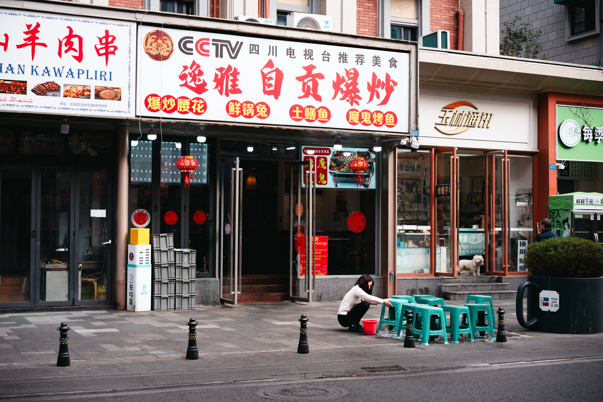 A person cleans teal plastic stools outside restaurants in Chengdu, China.
