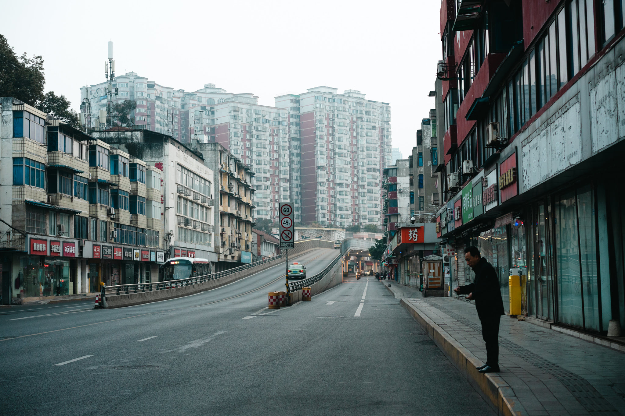 A mostly empty street in Chengdu, China, on a foggy morning; a man stands on the sidewalk.