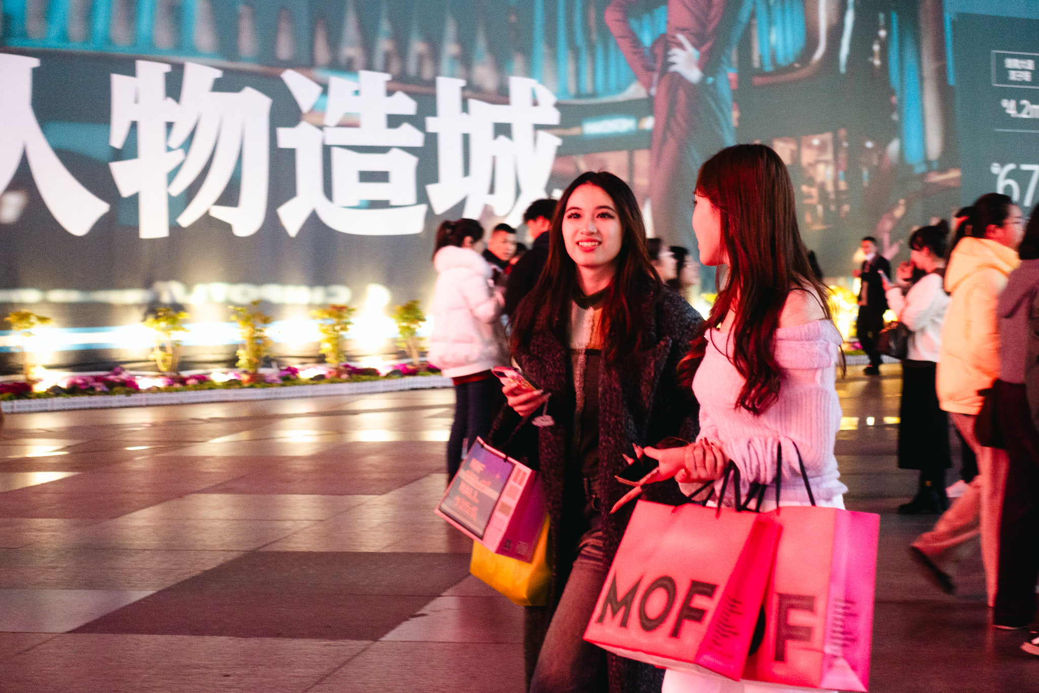 Two young women shopping at night in China, carrying pink shopping bags.