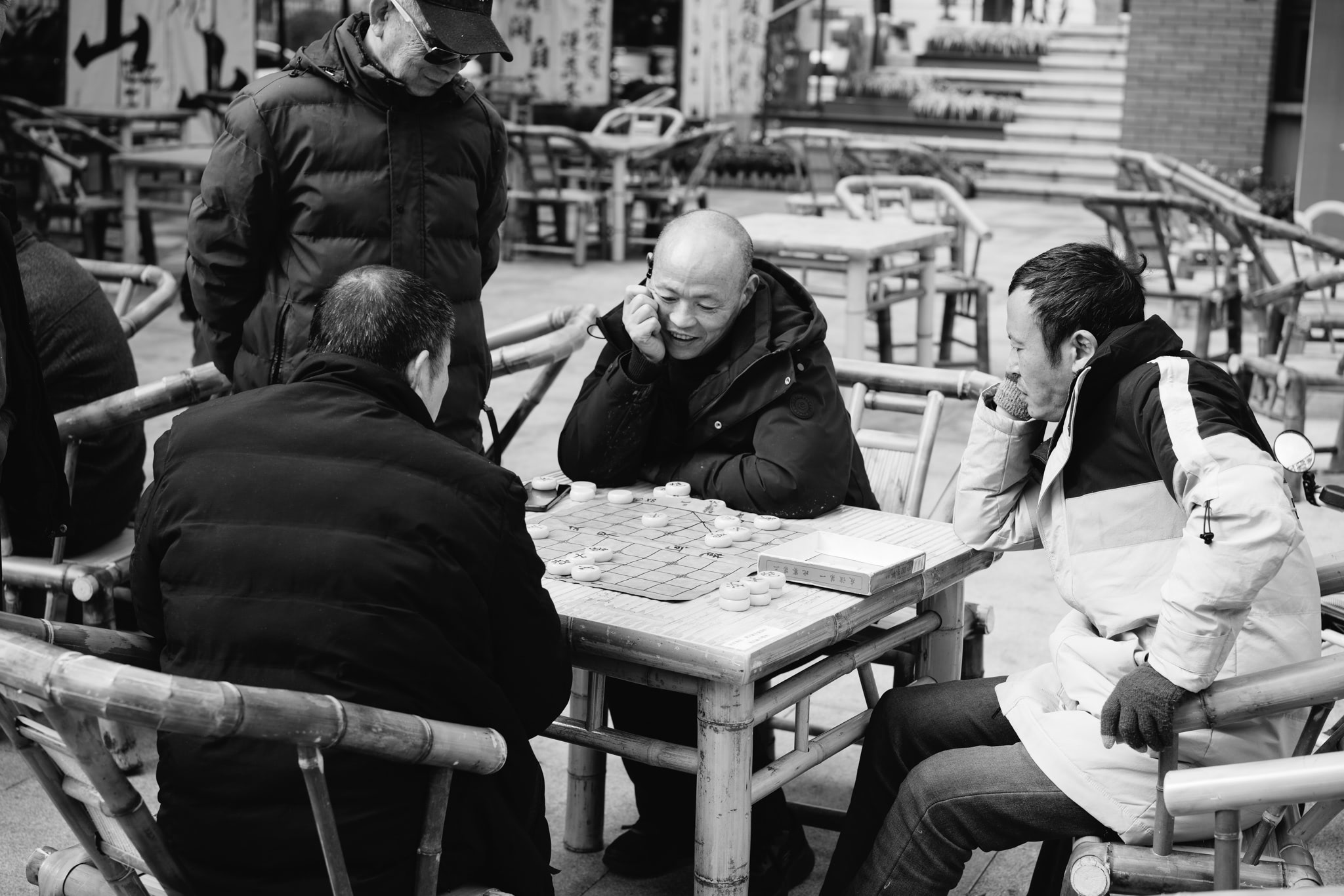 Three men playing Go at a bamboo table outdoors in Chengdu, Sichuan.