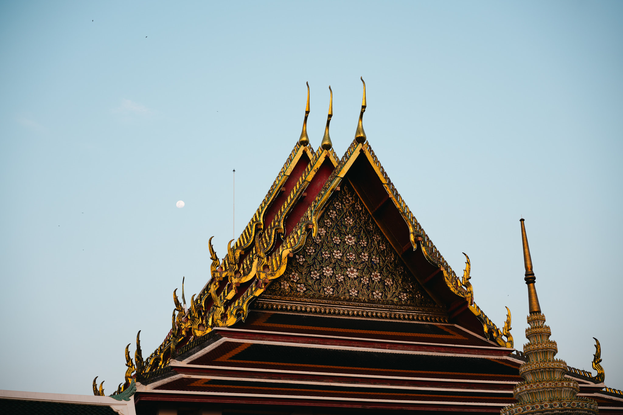 Ornate golden and red temple roof against a pale blue sky.