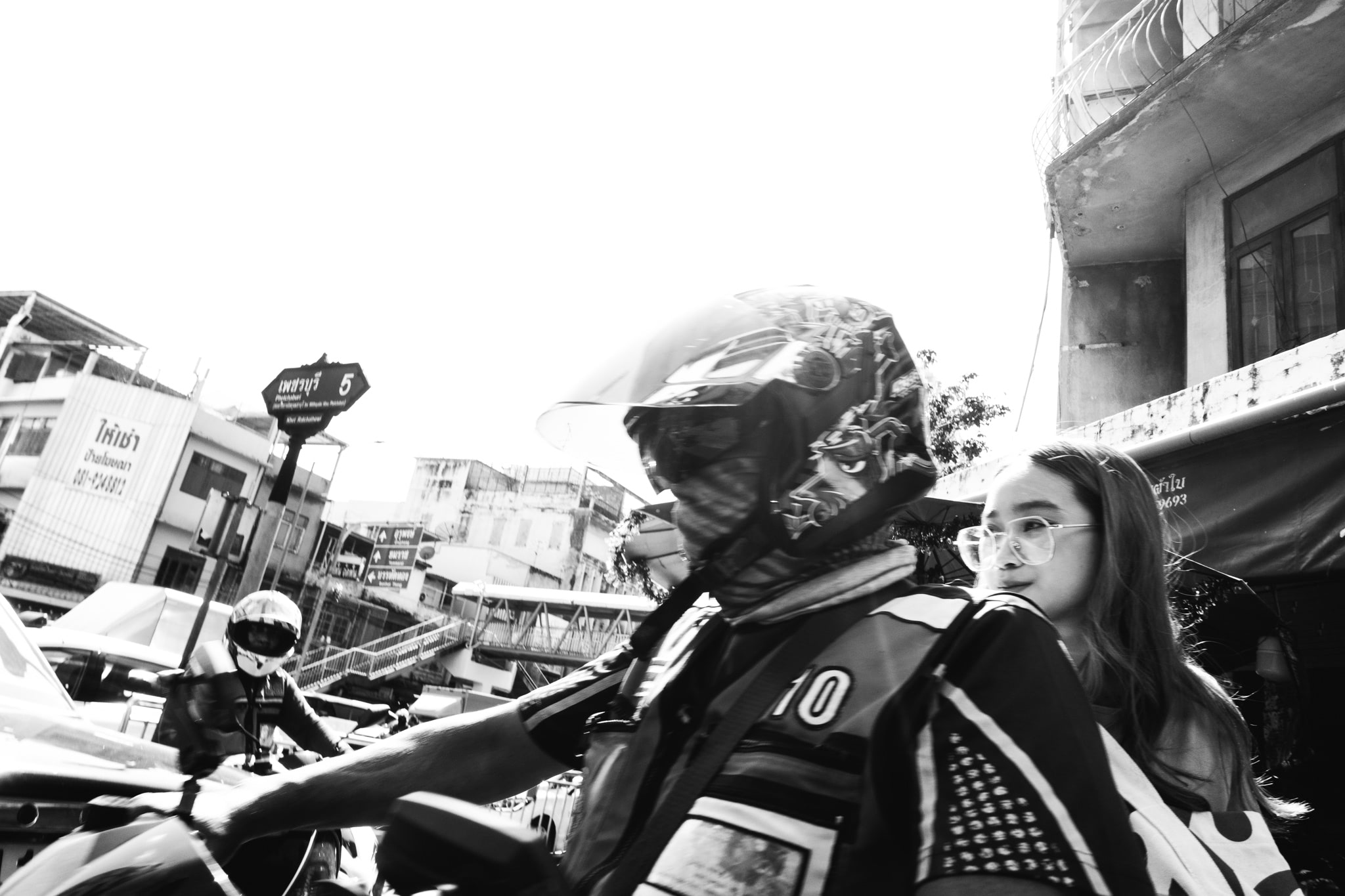 Black and white close-up of a motorcycle taxi driver with a passenger.