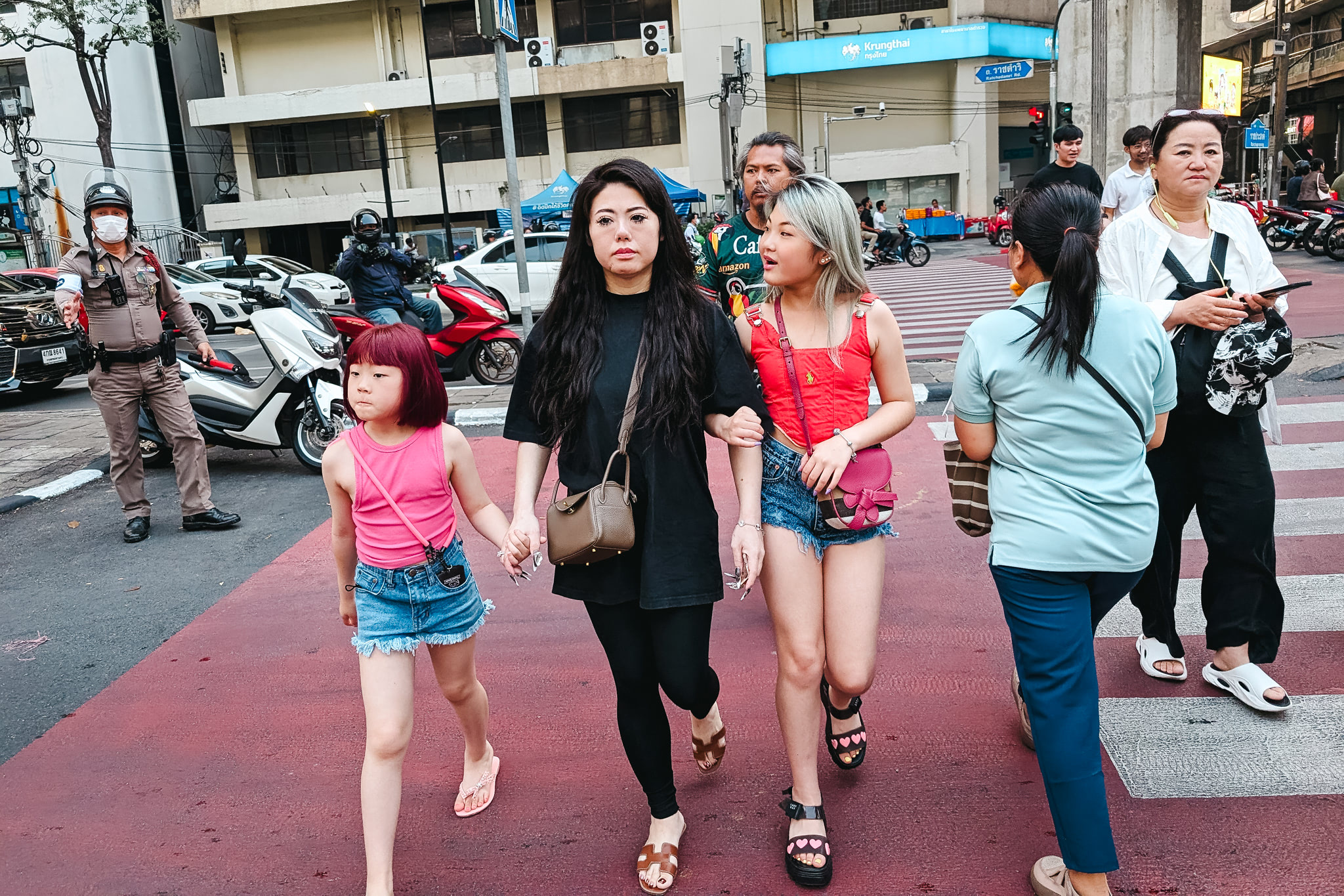 A mother and two daughters walking across a crosswalk in Bangkok, Thailand.