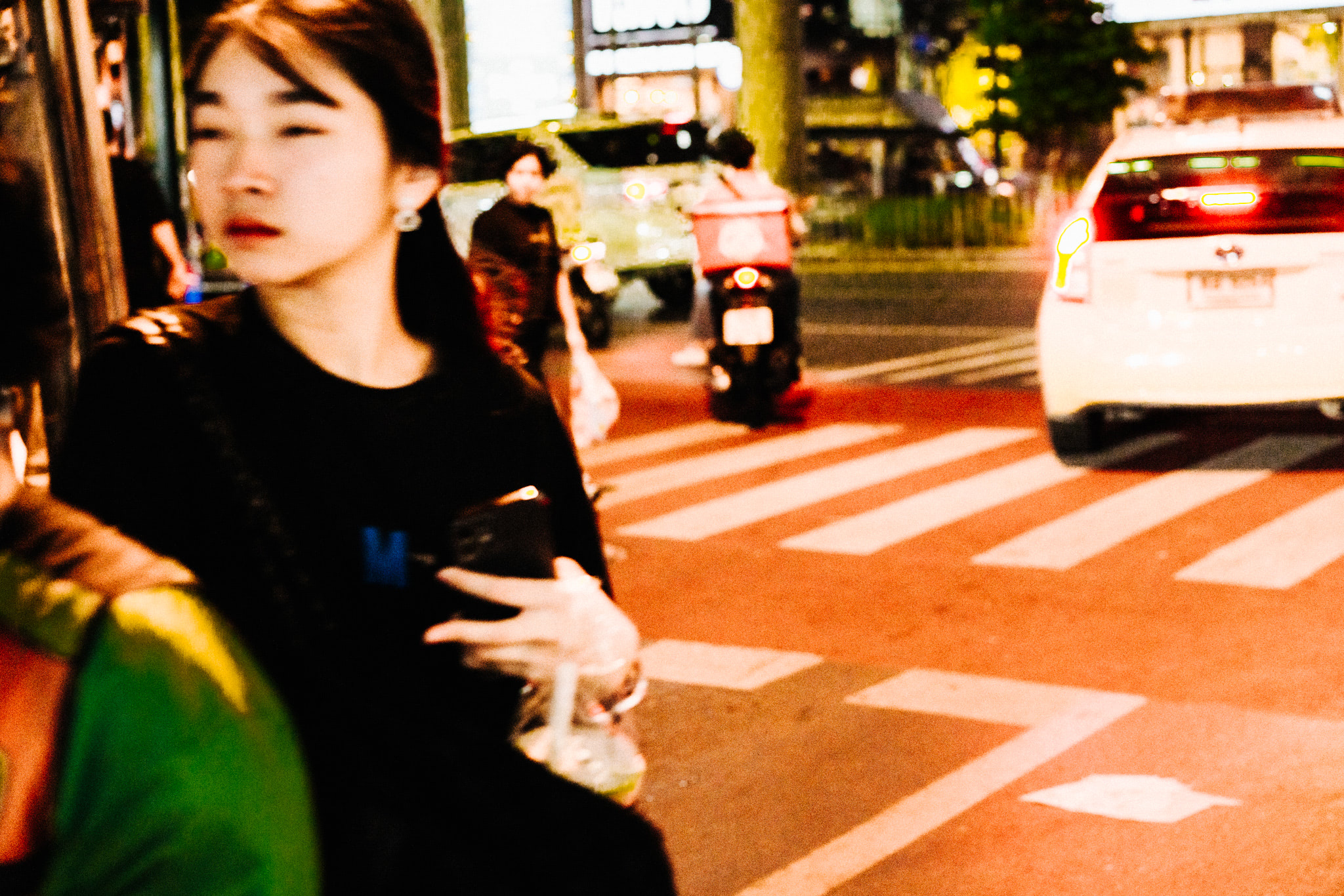 Blurry photo of a young woman at night in Bangkok, Thailand, standing near a crosswalk.
