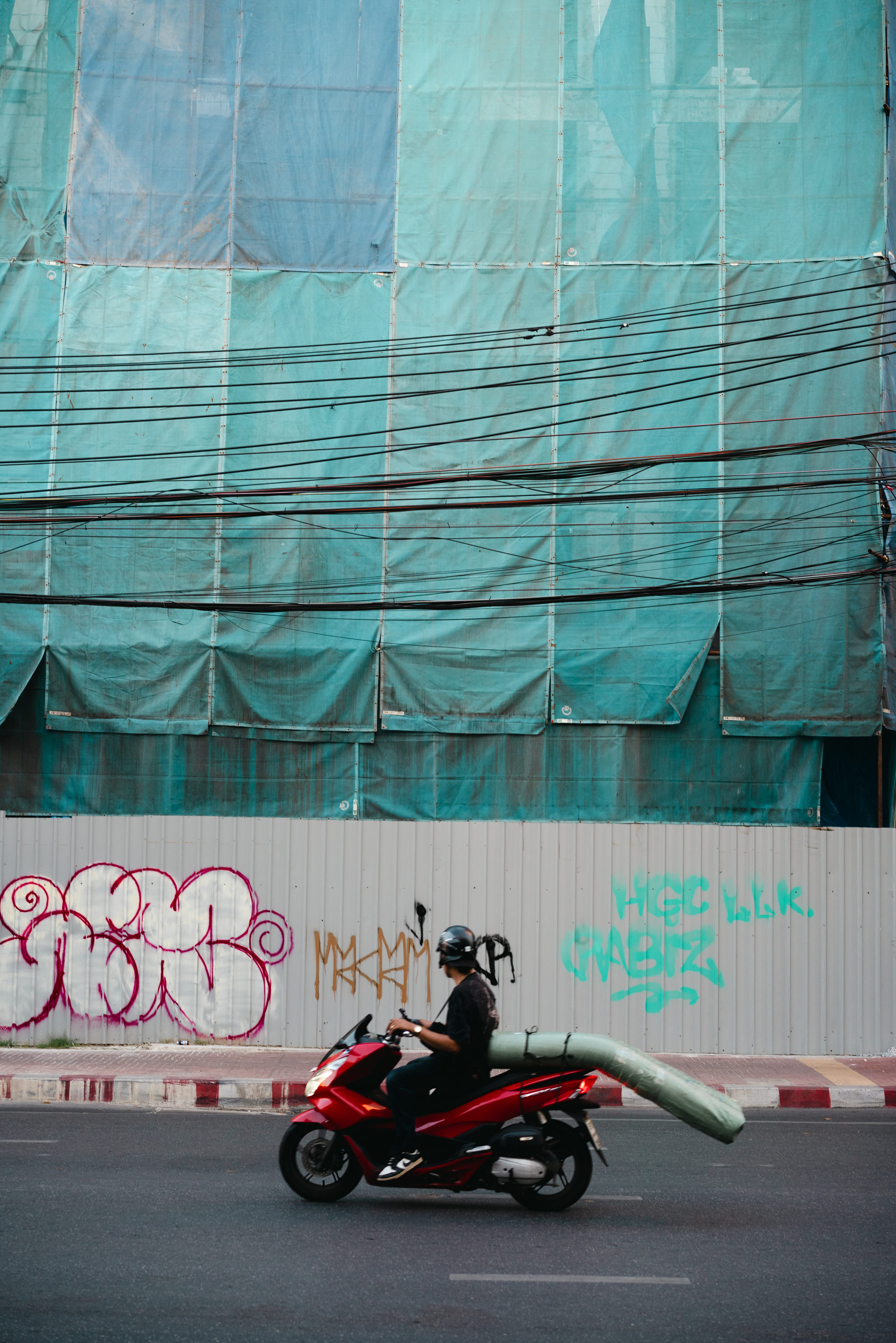 Person on red motorbike carrying a large object, driving past a building under construction.