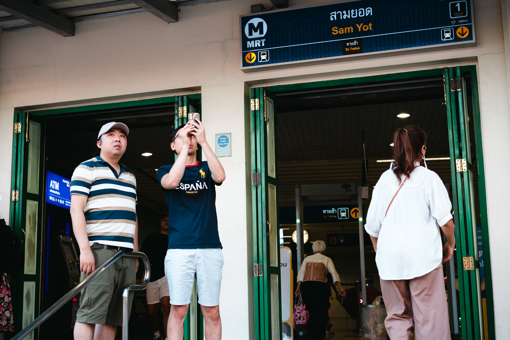 Three people stand outside the Sam Yot MRT station entrance in Bangkok.