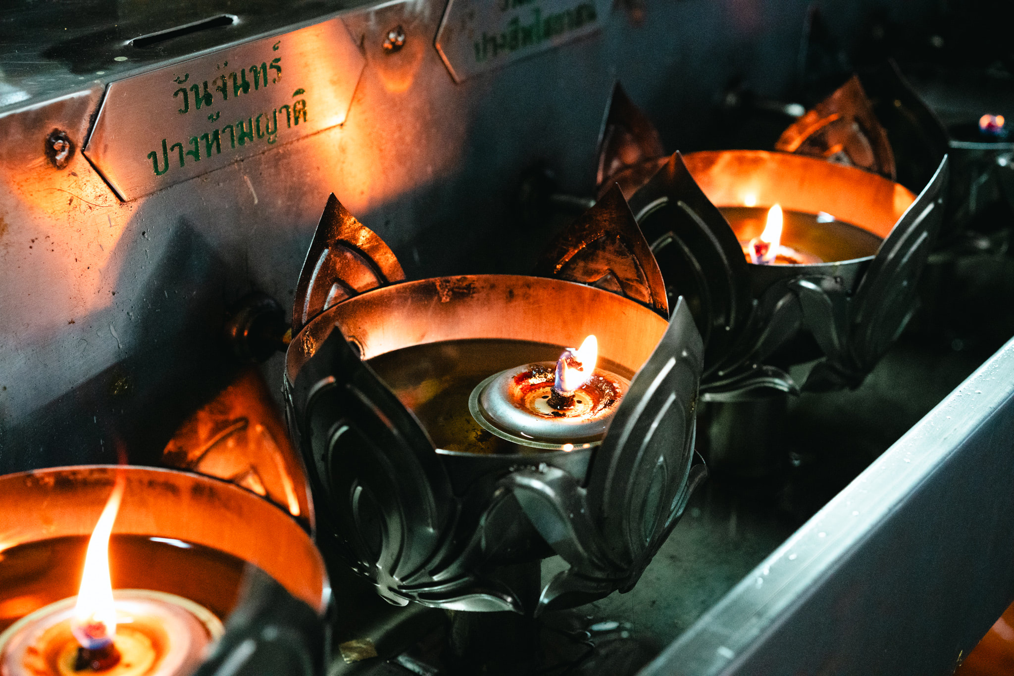 Lit oil lamps in ornate metal holders at a temple.