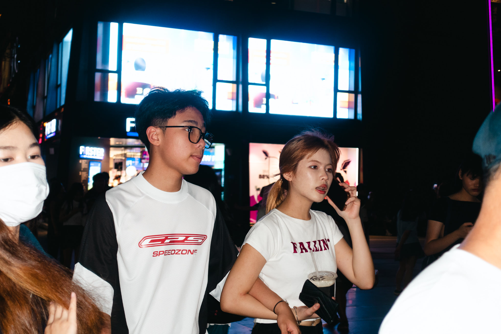 Two young people walk down a city street at night, the woman on the phone.
