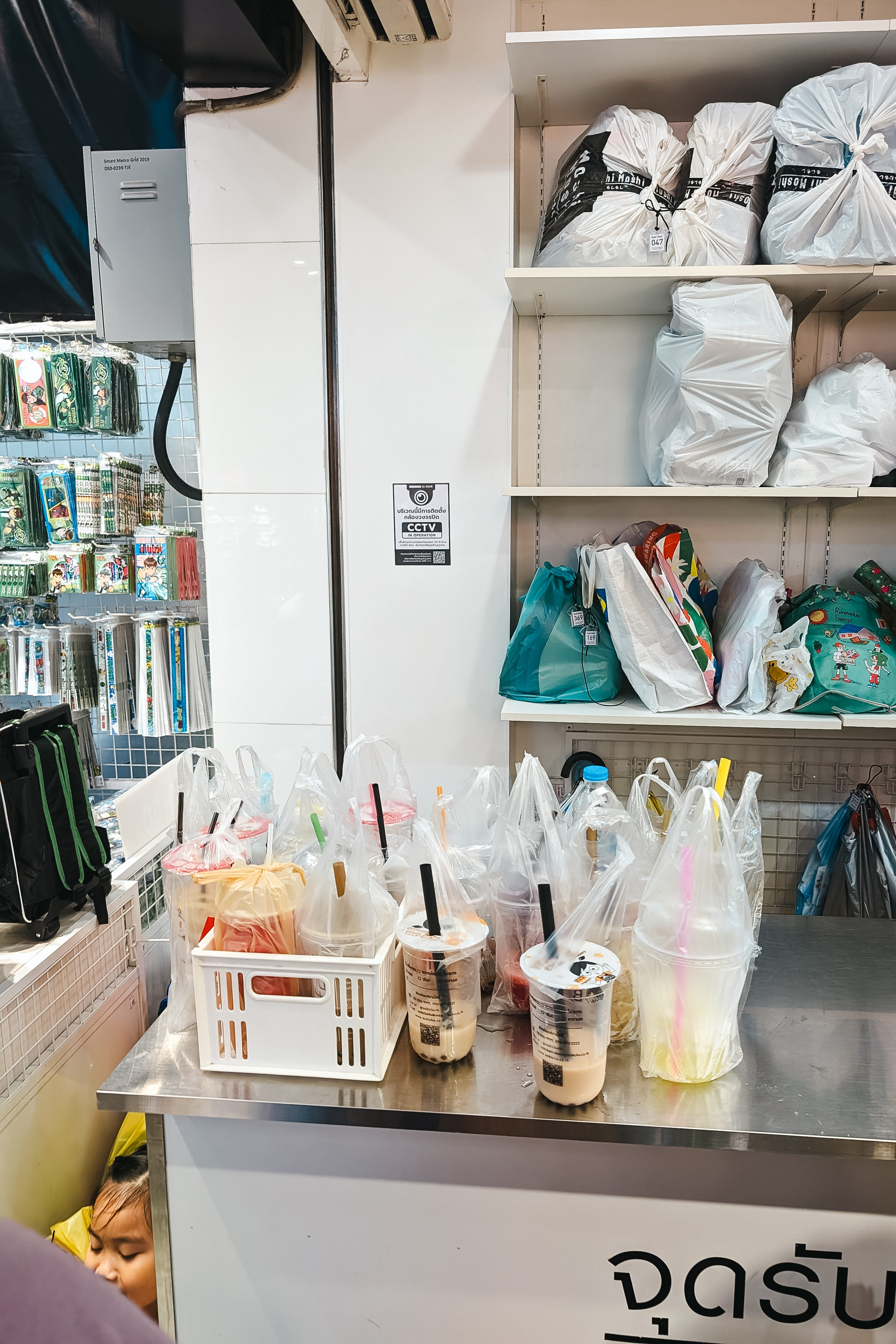 Multiple bubble tea drinks in plastic bags waiting outside a shop.