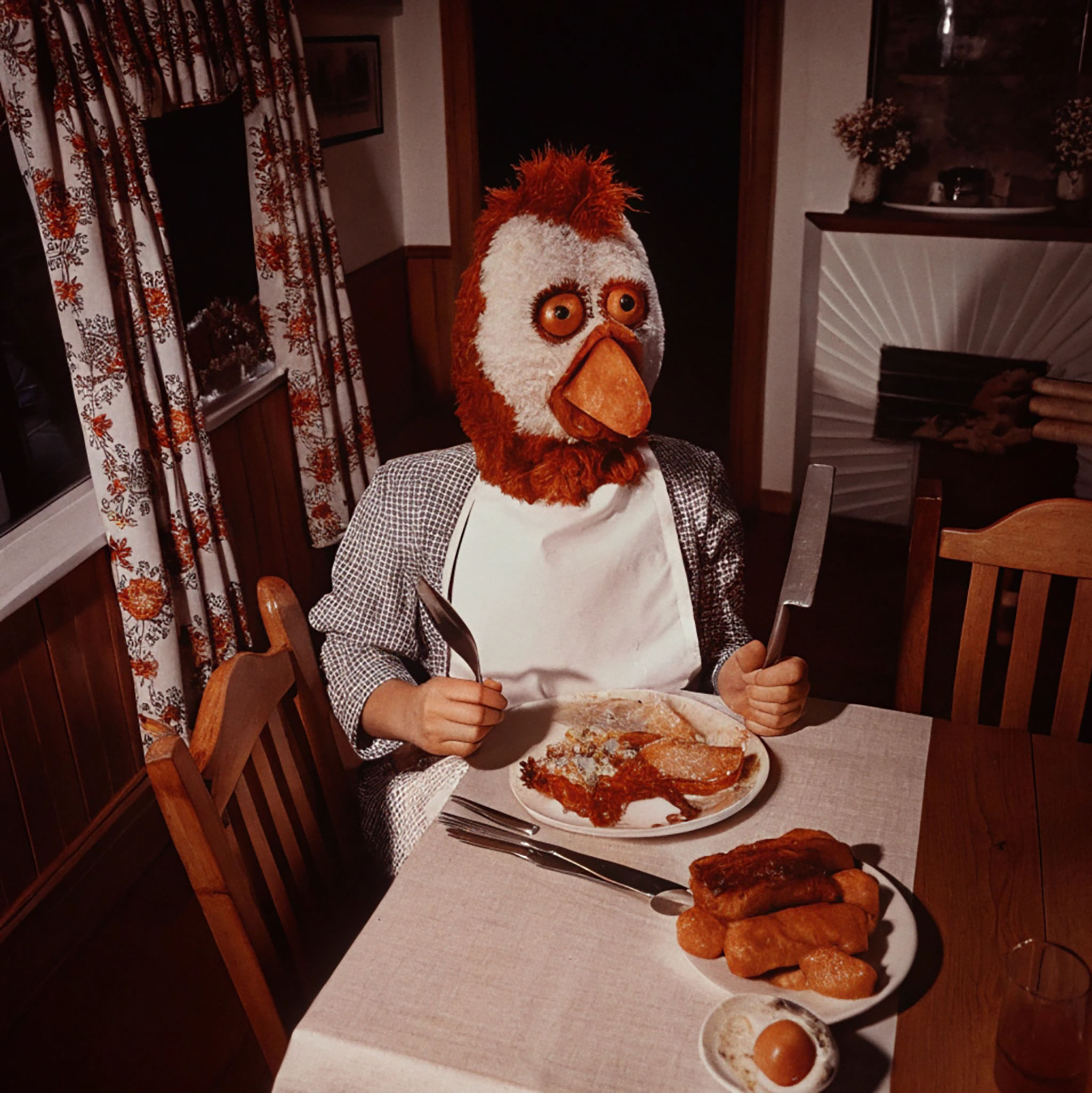 Anthropomorphic chicken in a mask eating breakfast.