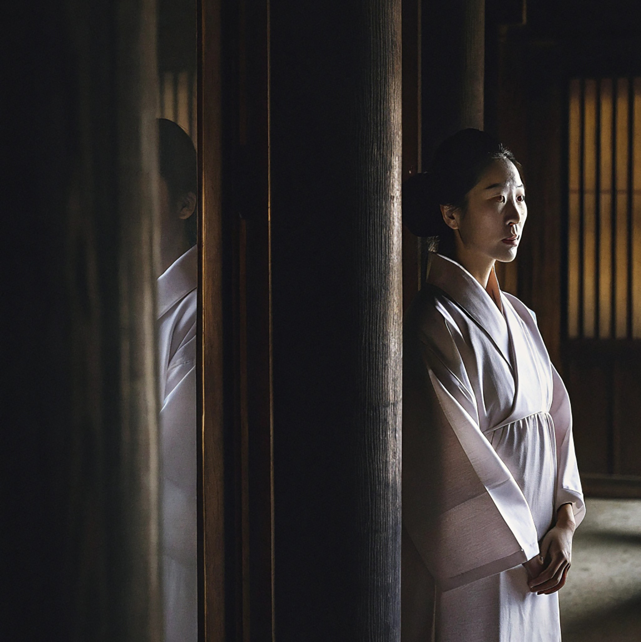 Korean woman in white hanbok standing near wooden pillars.
