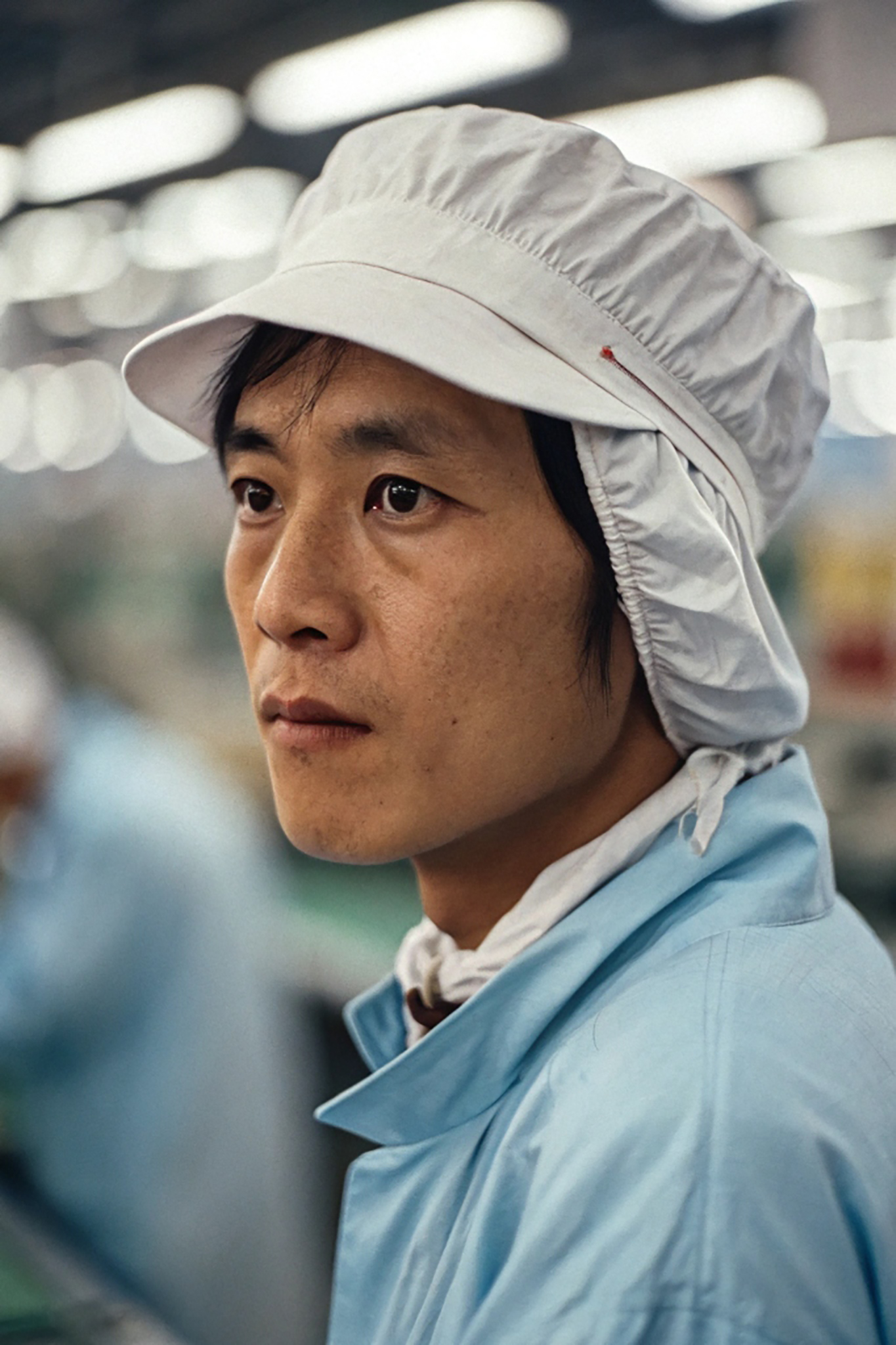 Close-up of a Taiwanese factory worker wearing a light blue uniform and white cap.