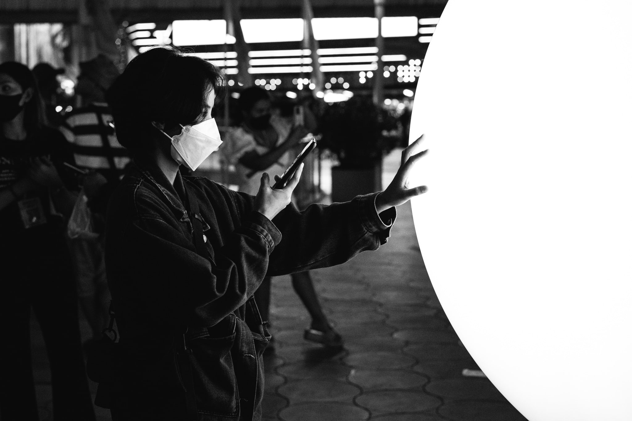 Person in mask using phone, touching large illuminated globe.