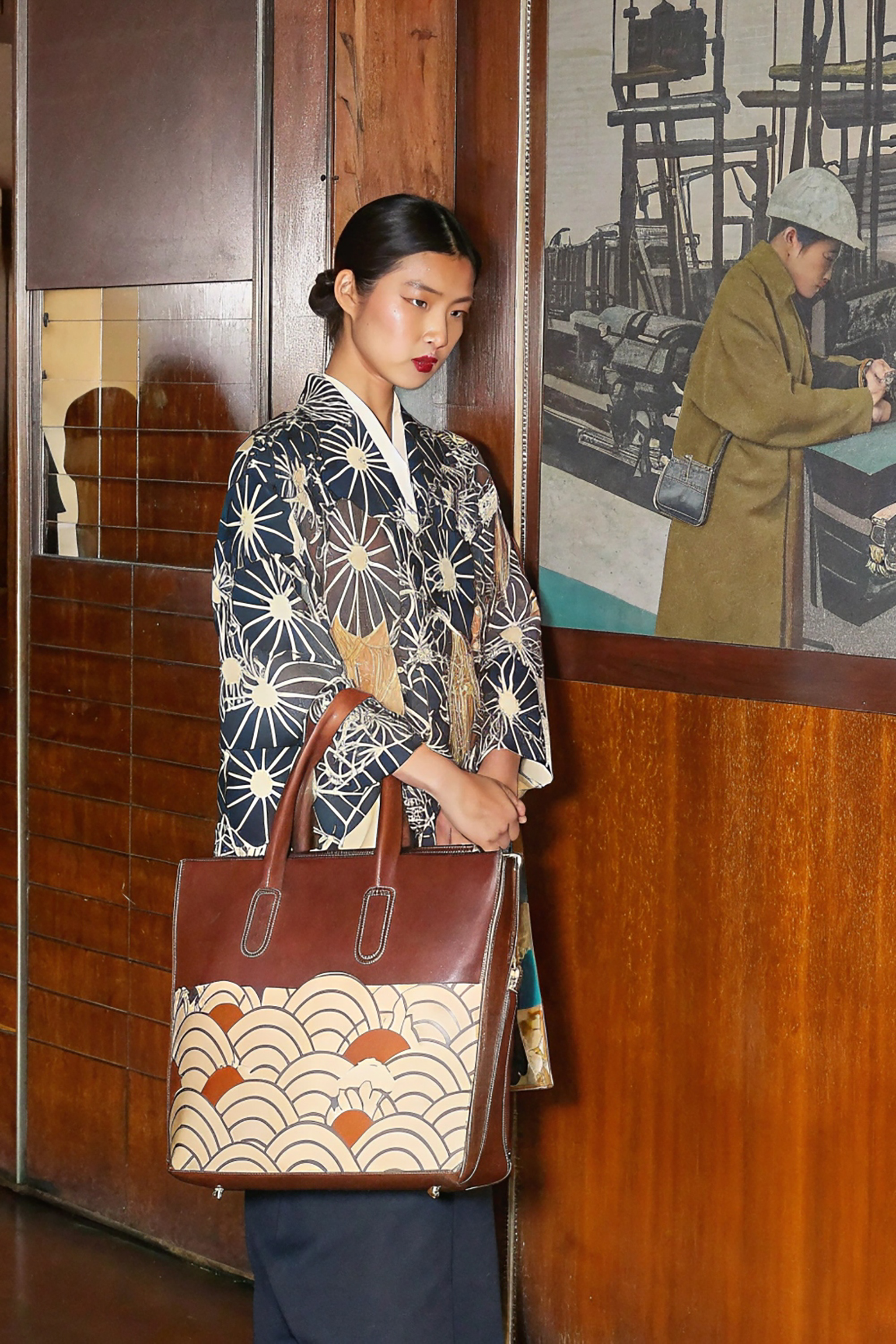 Woman in Japanese-inspired outfit holding brown leather handbag with wave pattern.
