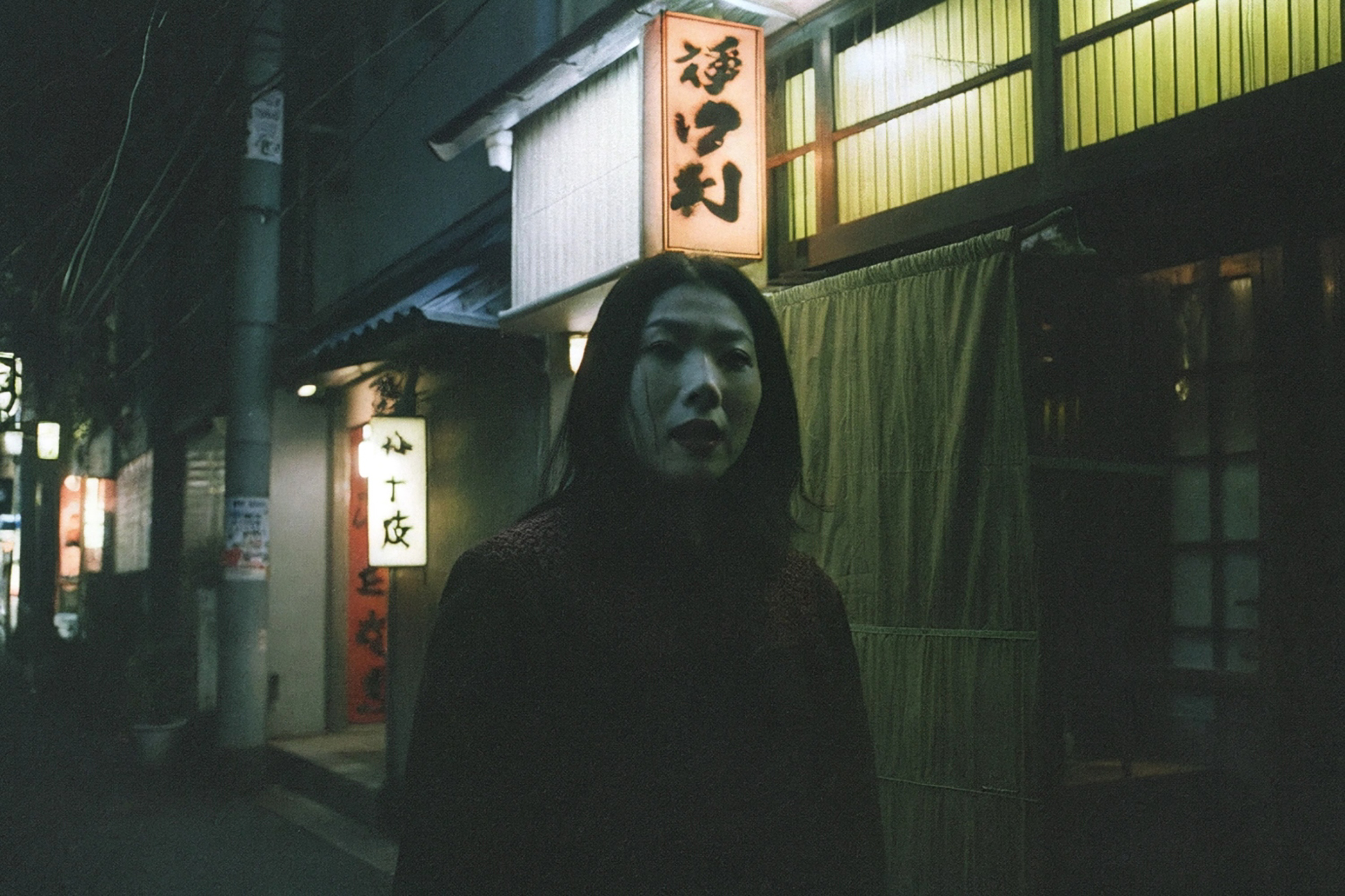 Woman standing on a dark Nagoya street at night.