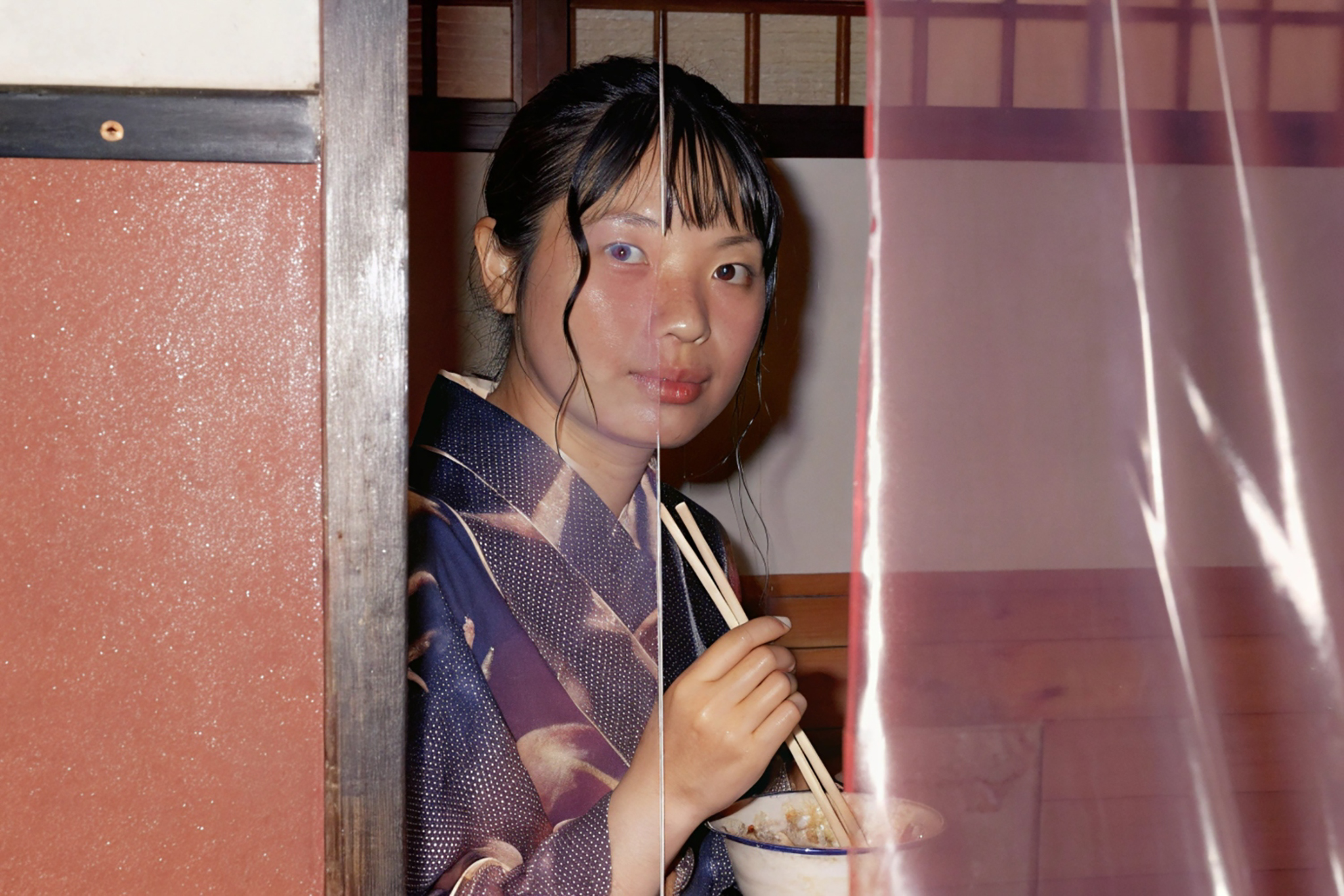 Woman in kimono eating ramen, partially obscured by a curtain.