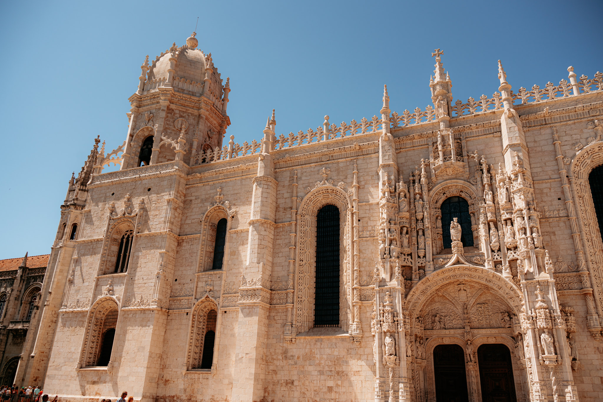 Jerónimos Monastery exterior, ornate stone facade with detailed carvings and a bell tower.