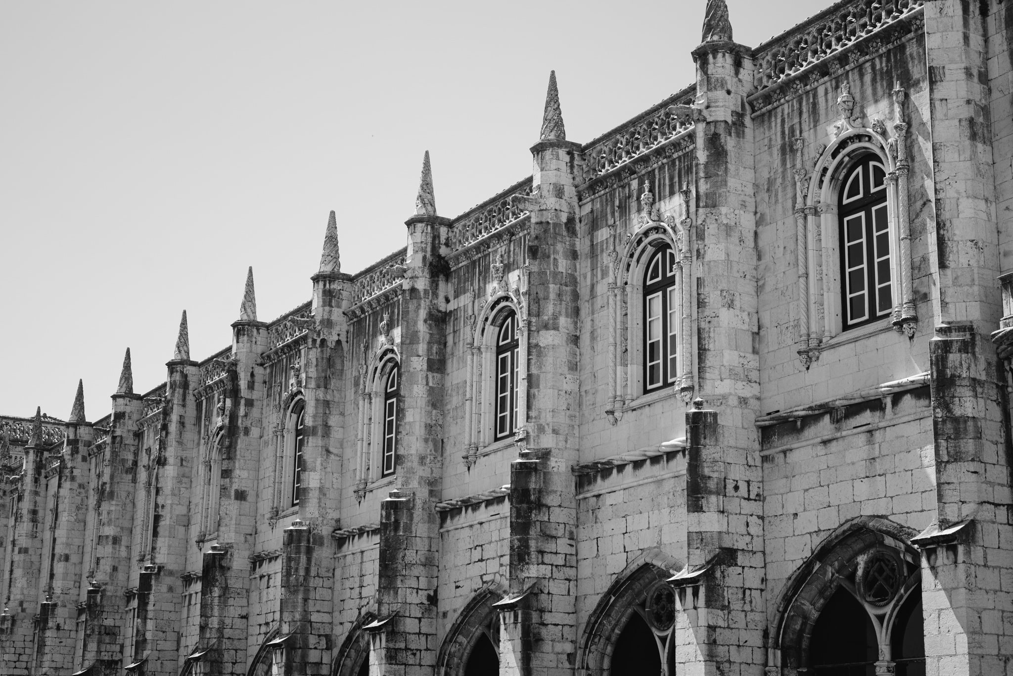 Black and white photo of Jerónimos Monastery exterior wall with ornate detailing and multiple windows.