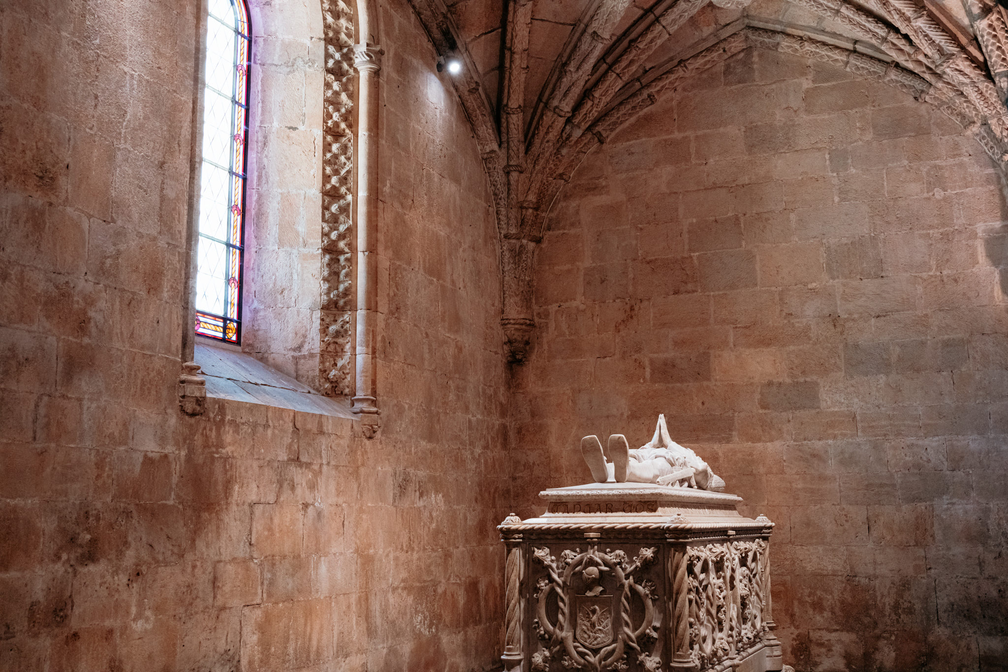 Ornate stone tomb with a recumbent effigy in a Jerónimos Monastery chapel.