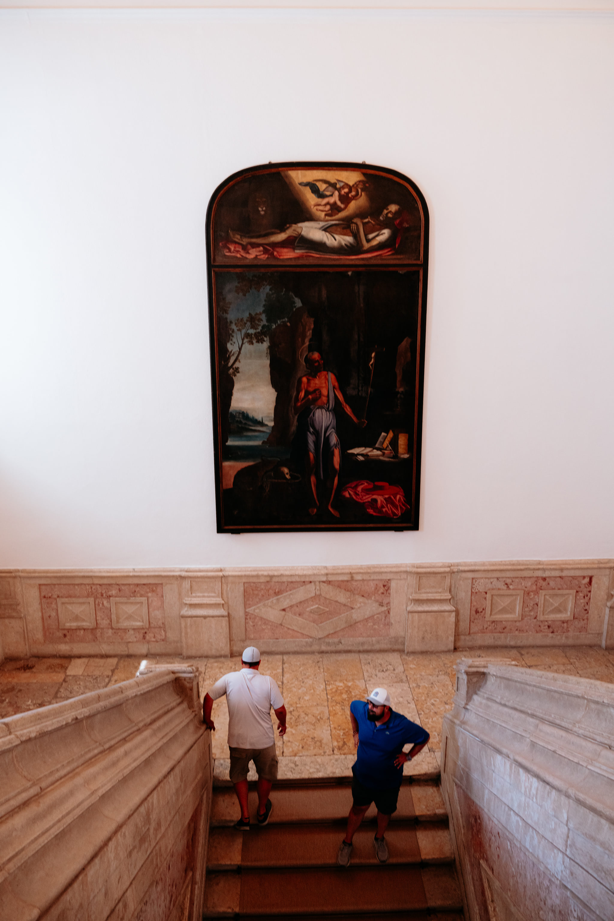 Two men on a stone staircase below a large painting depicting a religious scene.