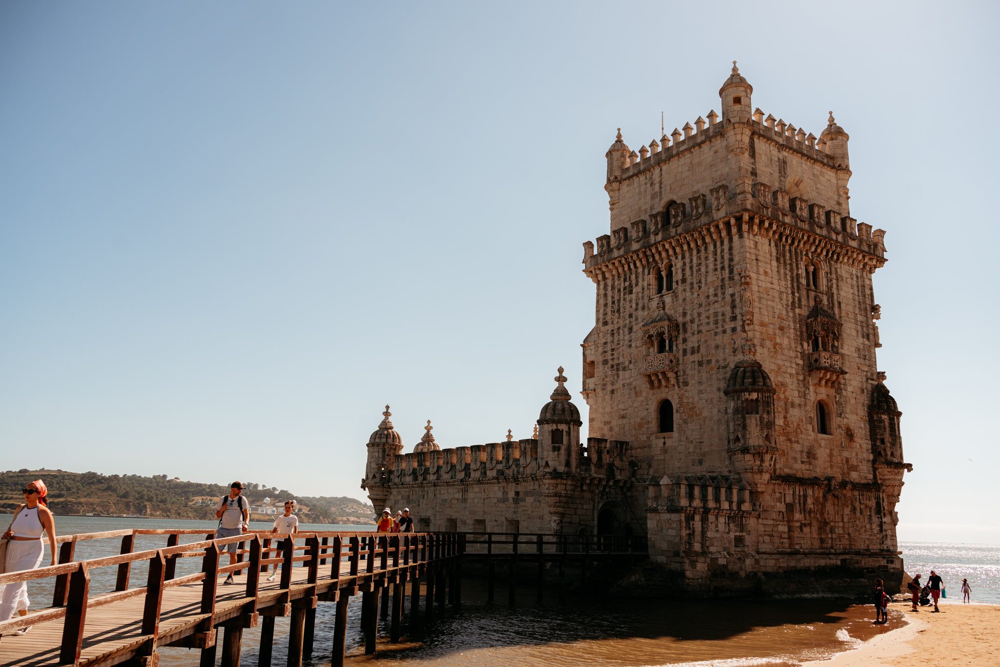 Belém Tower in Lisbon, Portugal, with people walking on a wooden boardwalk.