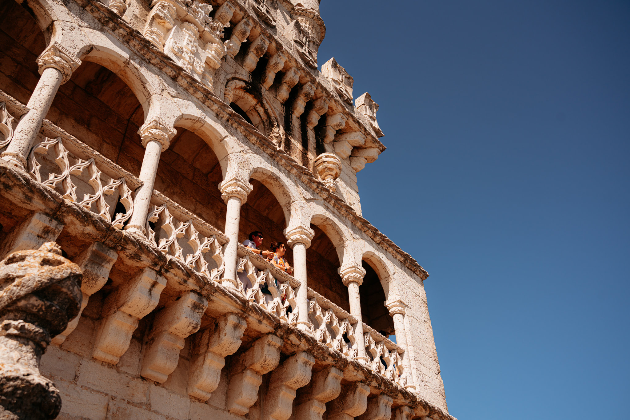 Belém Tower in Lisbon, Portugal, with two tourists on a balcony.