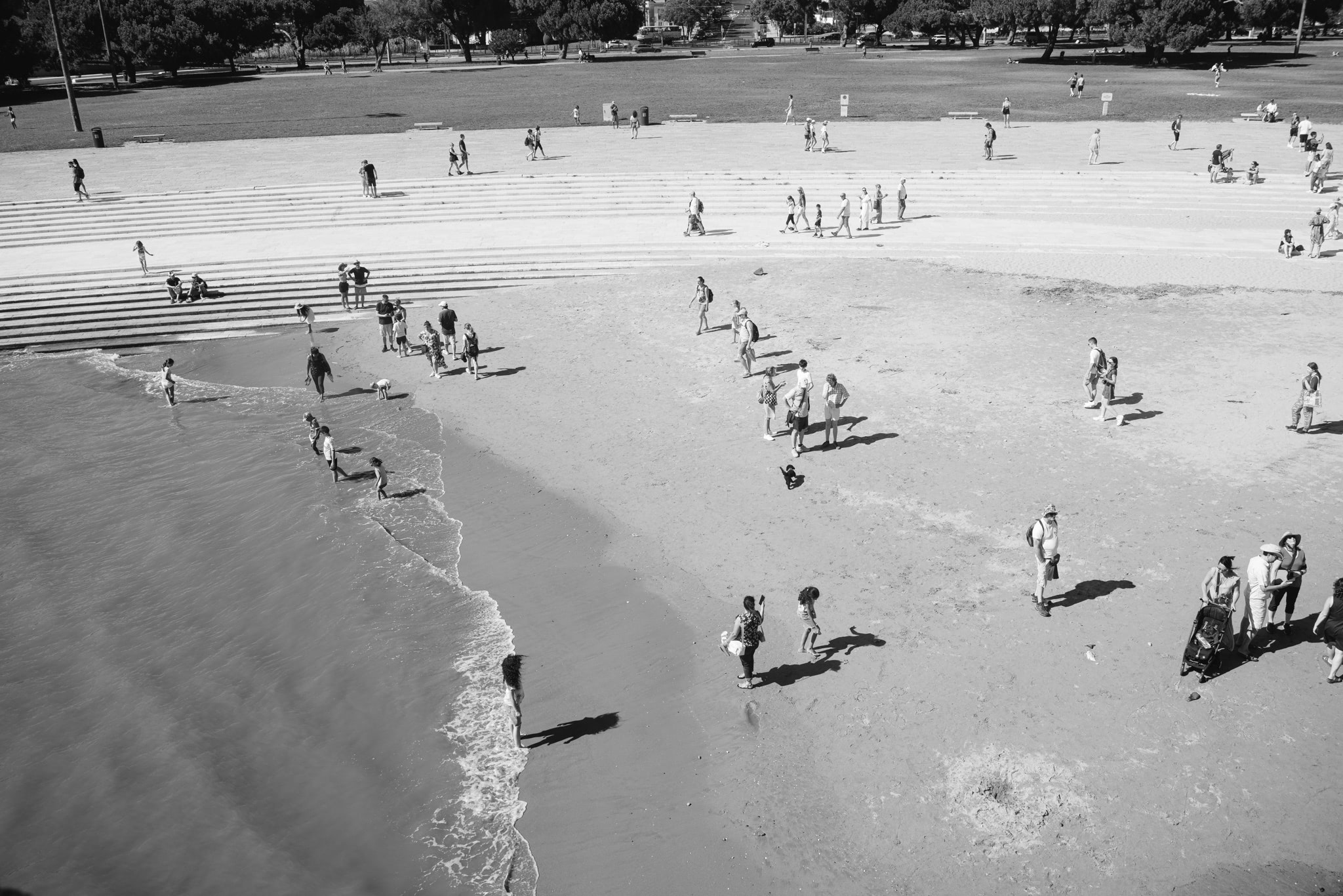 Black and white aerial view of people relaxing on a beach and nearby steps.