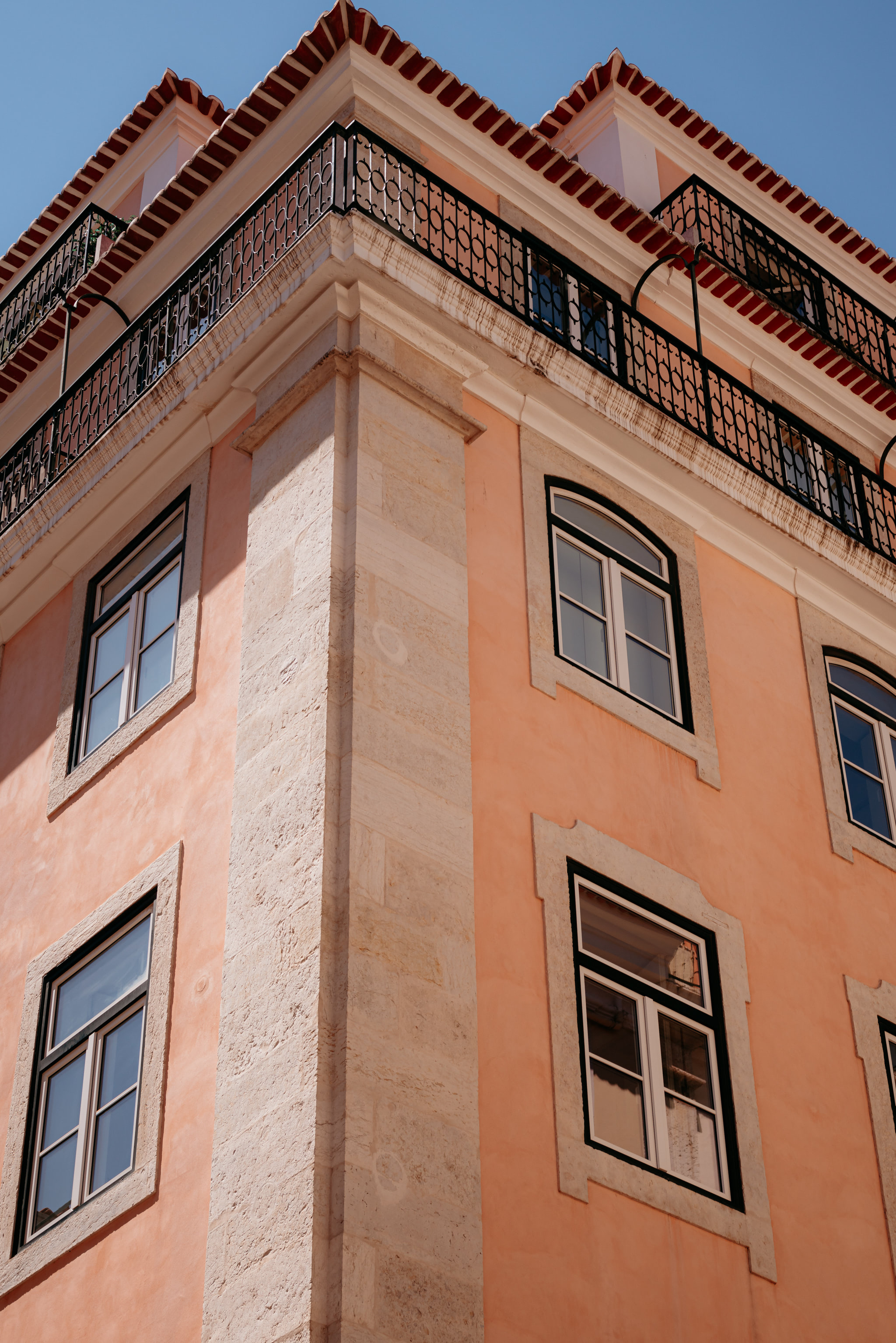 Low-angle view of a peach-colored building in Lisbon, Portugal, with black iron balconies and windows.