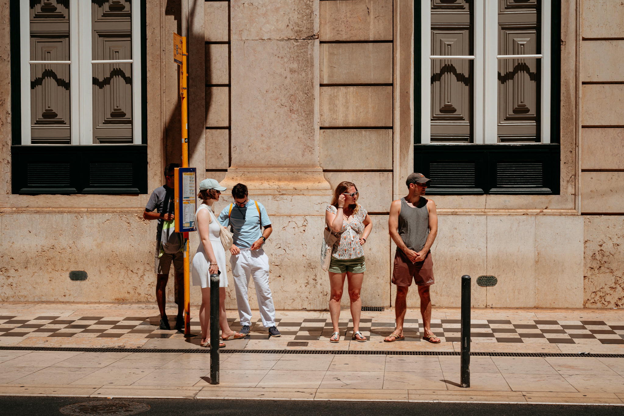 Four people waiting at a sunny Lisbon bus stop.