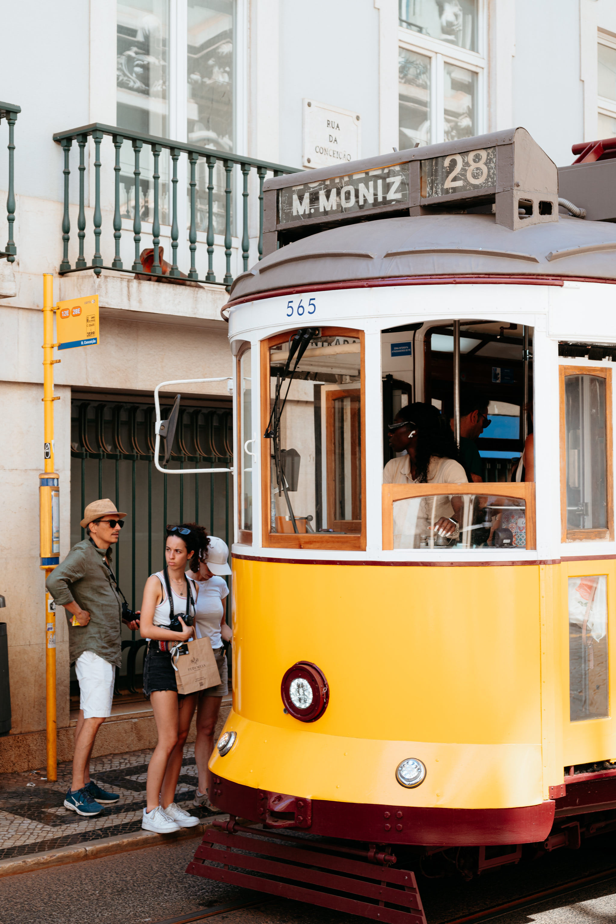 Yellow Lisbon tram #565, route 28, at a stop.