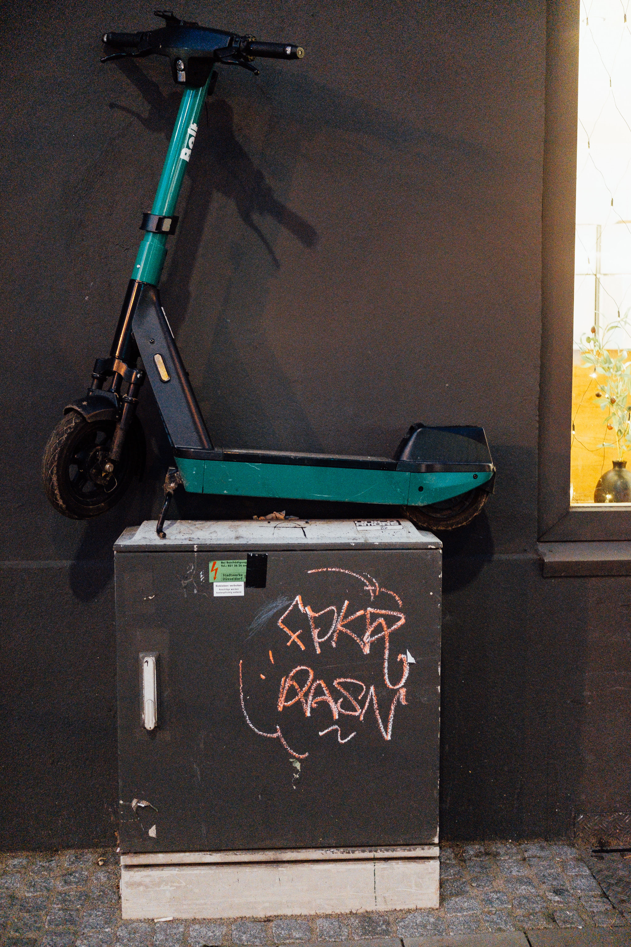 Teal Bolt rental scooter on a gray box with graffiti.