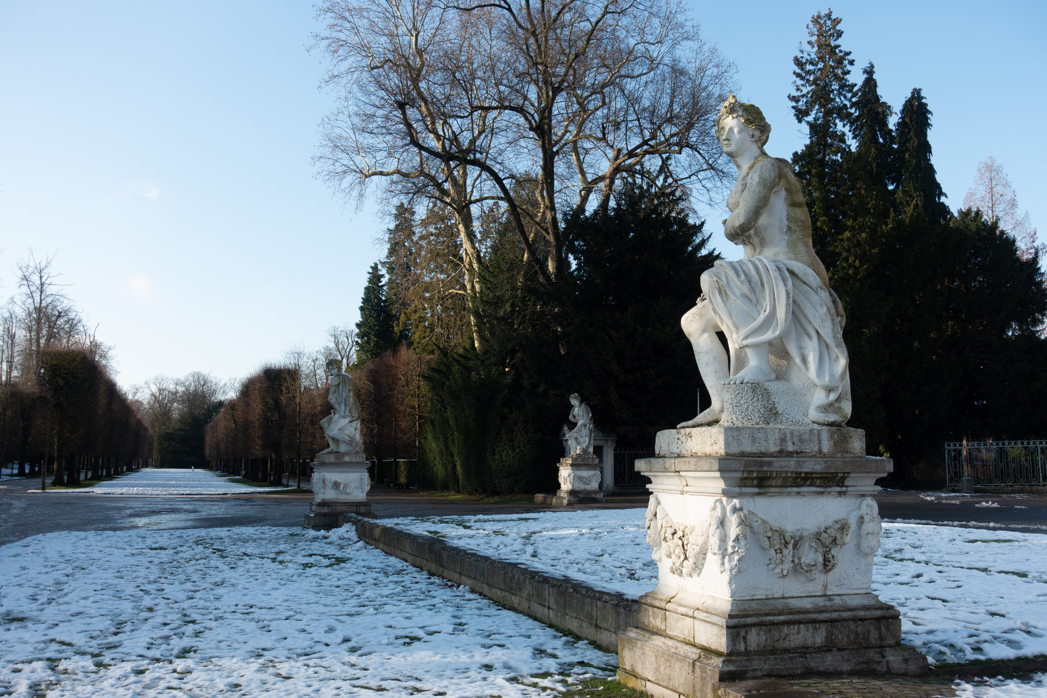 Snow-covered park with classical statues.