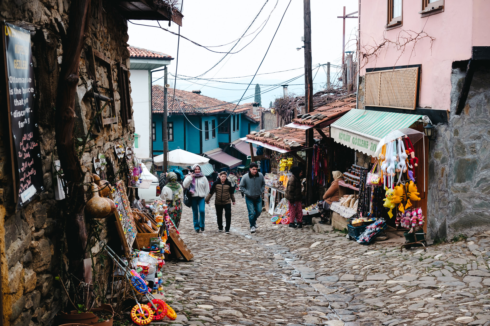 People walk down a cobblestone street lined with shops.