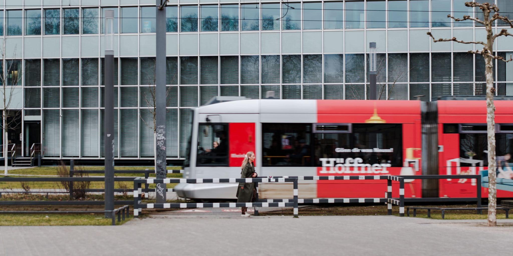 A woman walks past a blurred red and white tram in front of a modern building.