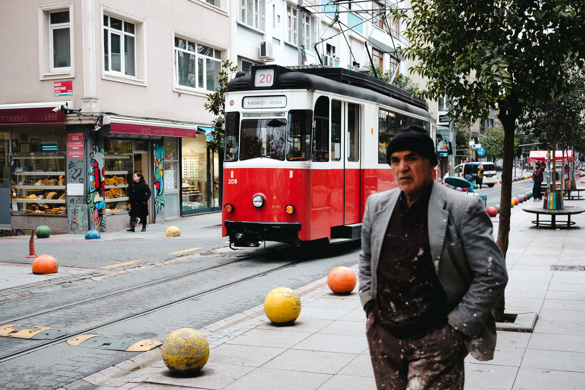 Red and white tram in Istanbul, with a man in a paint-splattered suit in the foreground.