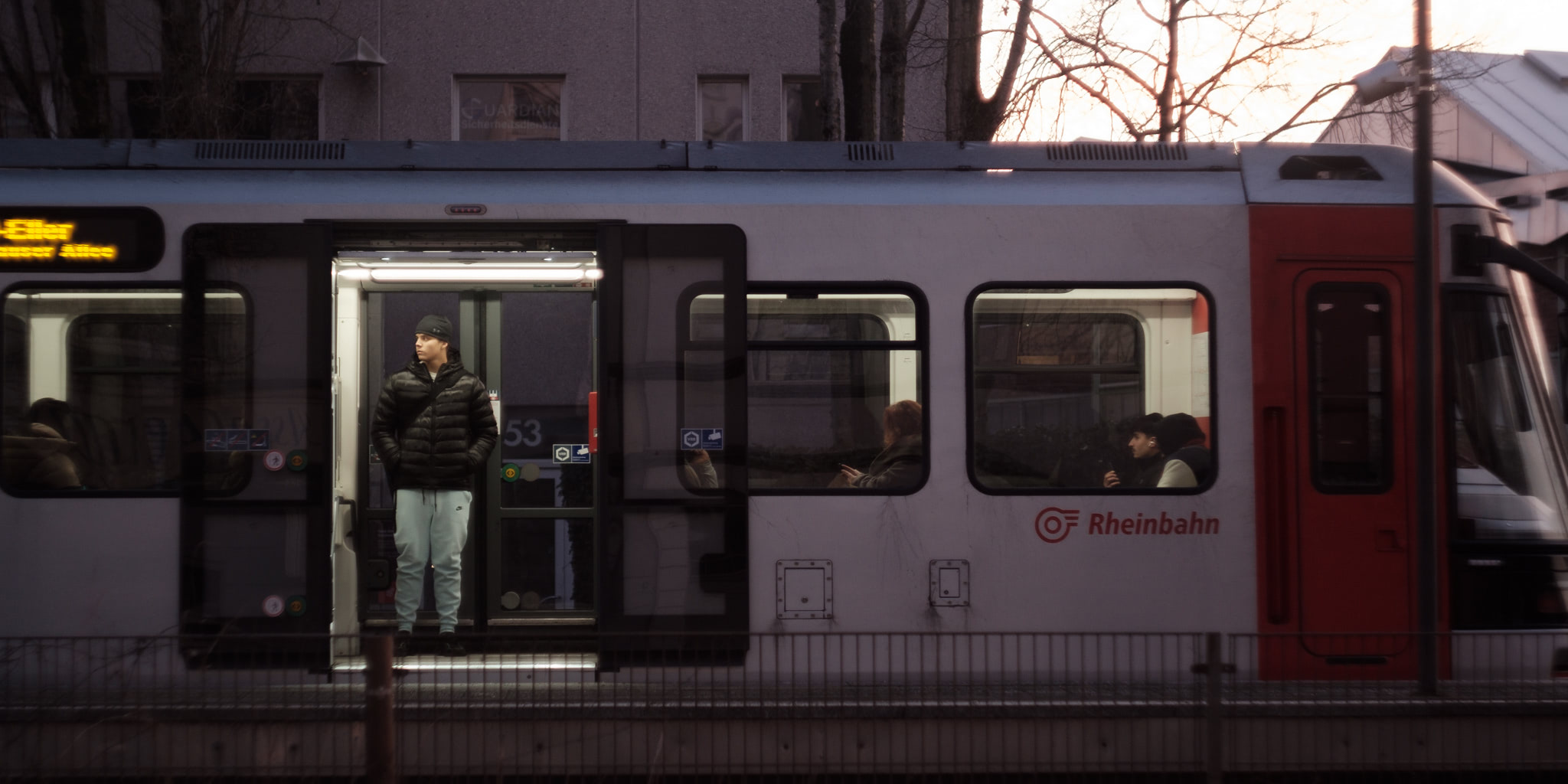 A young man stands in the open doorway of a Rheinbahn train.