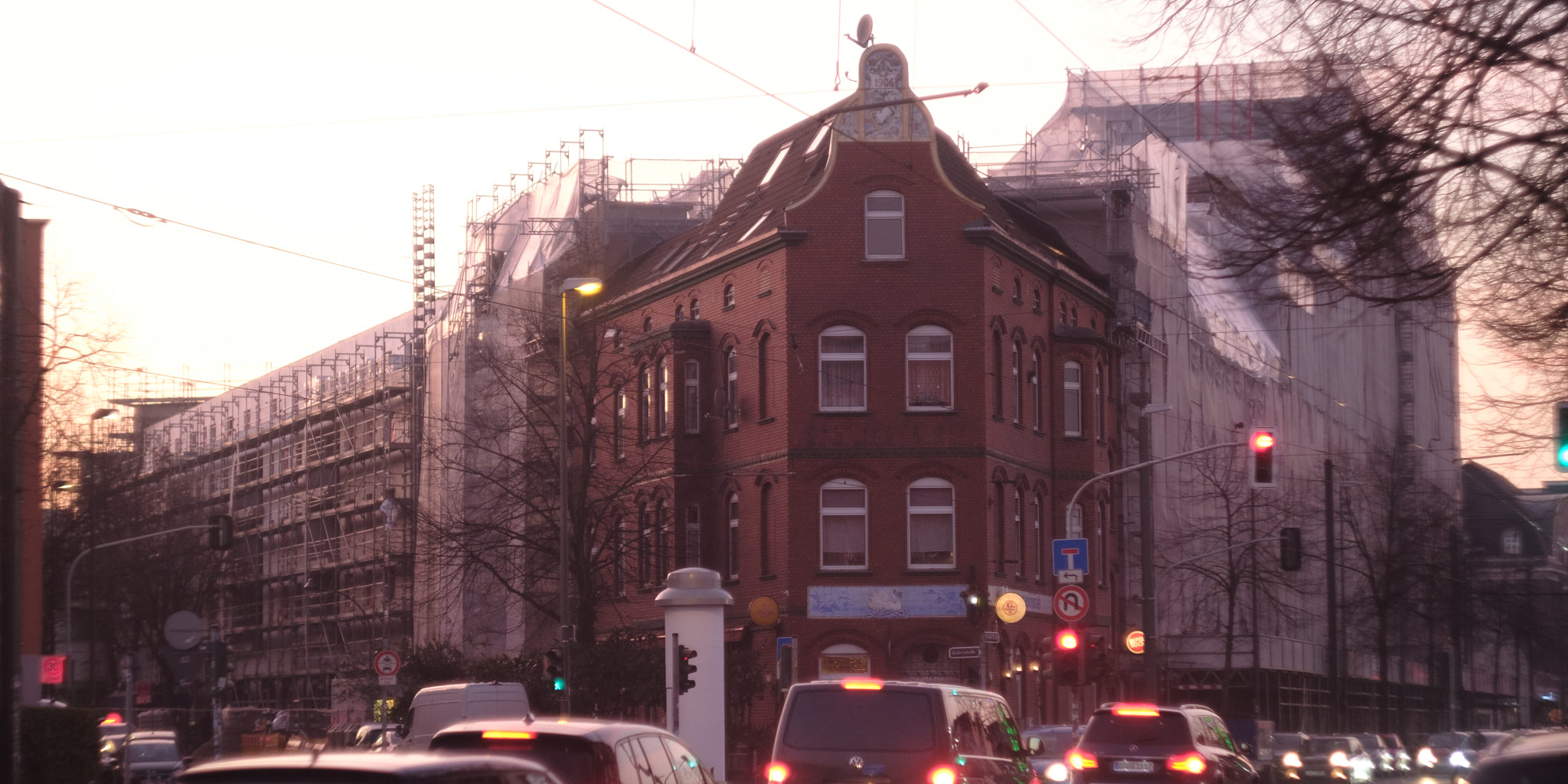 Street scene with red brick buildings in Germany, some under construction with scaffolding. Cars are lined up at an intersection with traffic lights.