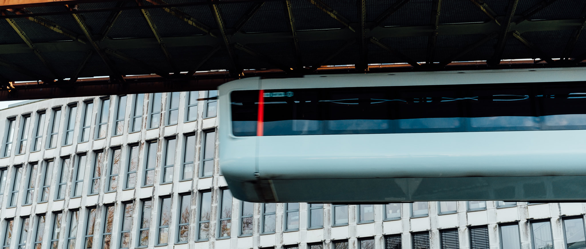 A suspended railway car speeds past a building with many windows.