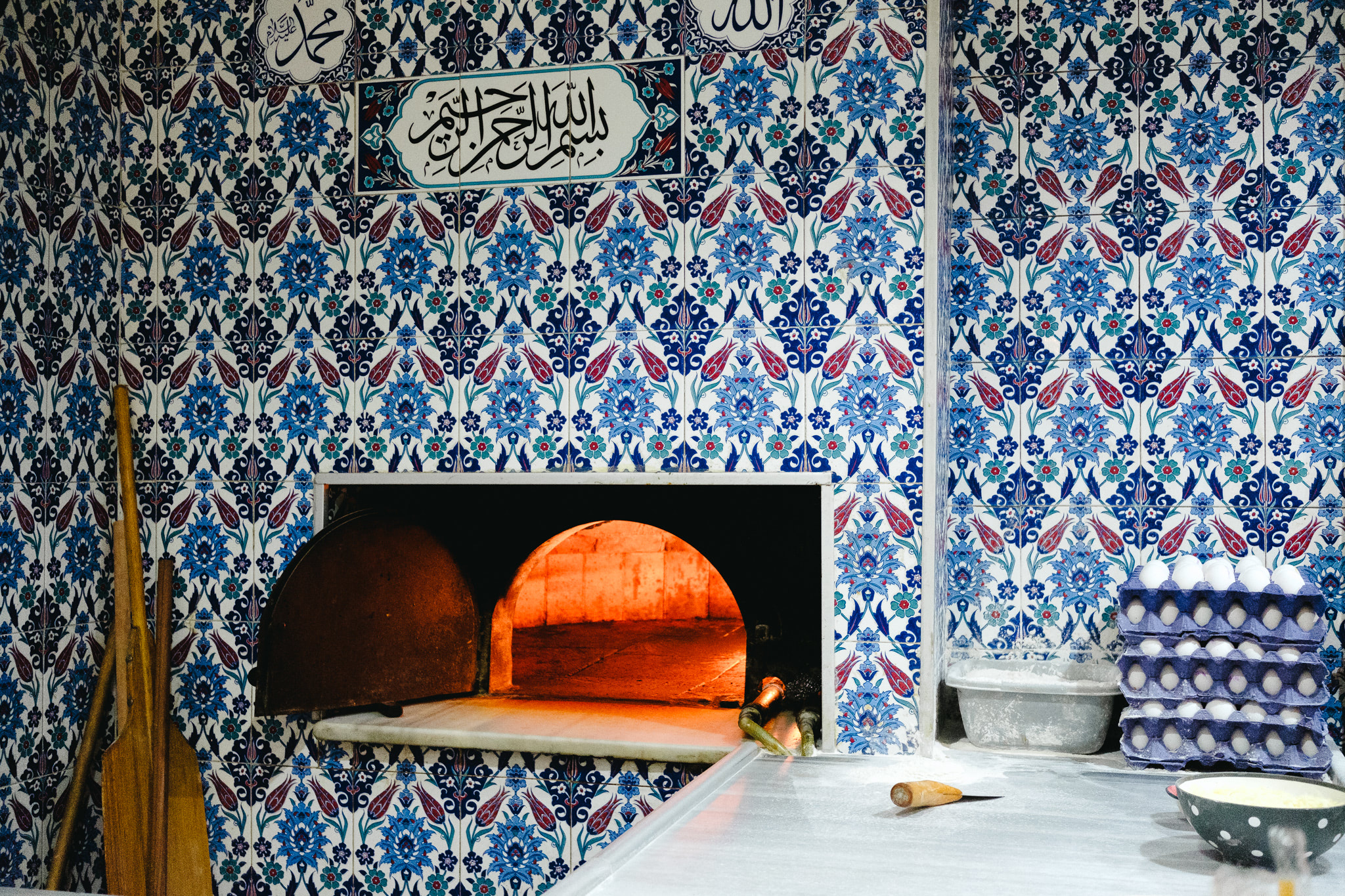 Interior of a bakery with a tiled wall, oven, and baking tools.